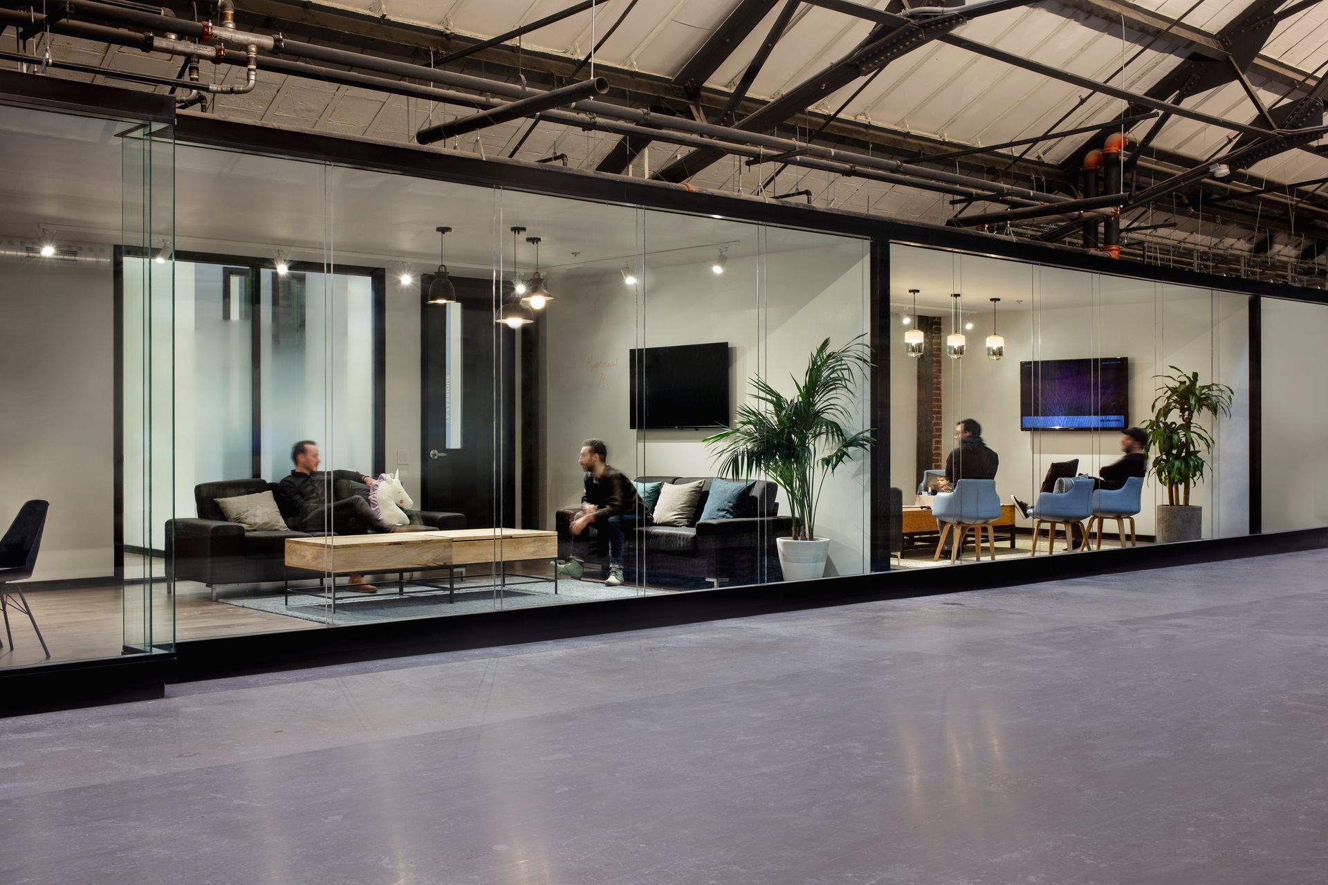 Vue intérieure d'un bureau moderne avec des cloisons vitrées, des canapés et des personnes au travail.