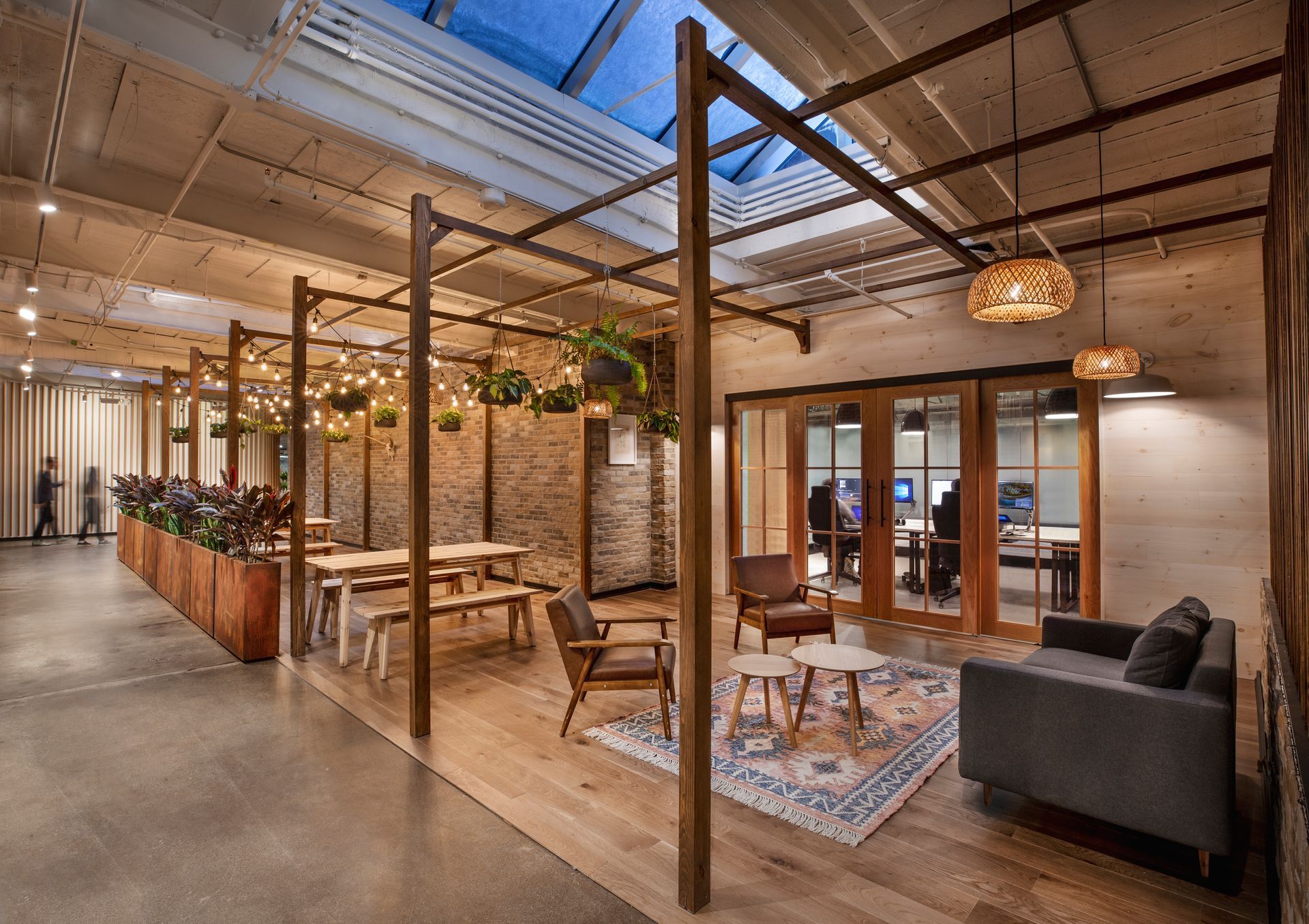 Espace de bureau intérieur avec sièges, poutres en bois, puits de lumière et plantes suspendues.