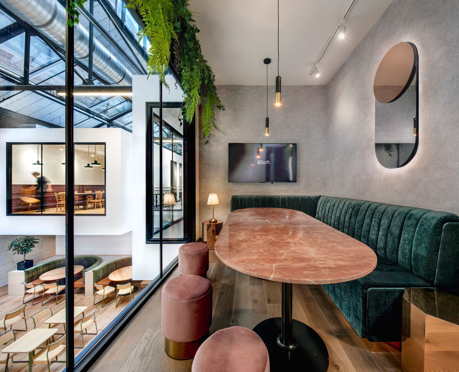 Un espace de détente moderne avec une longue table, des banquettes vertes et une grande fenêtre donnant sur un autre espace de travail.