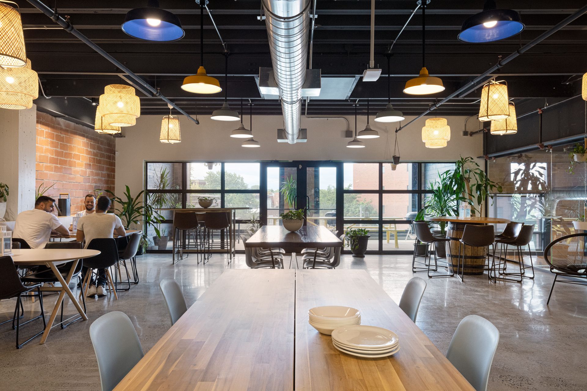 Bureau moderne à aire ouverte avec de grandes fenêtres, des tables et un éclairage varié. Les gens sont assis et travaillent.