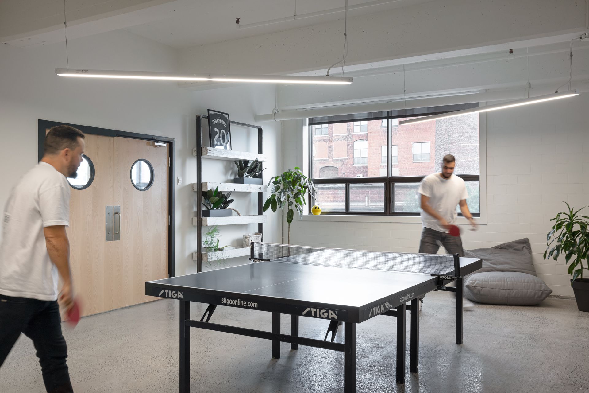 Deux personnes jouent au ping-pong dans un bureau lumineux. L'une d'elles s'apprête à frapper la balle.