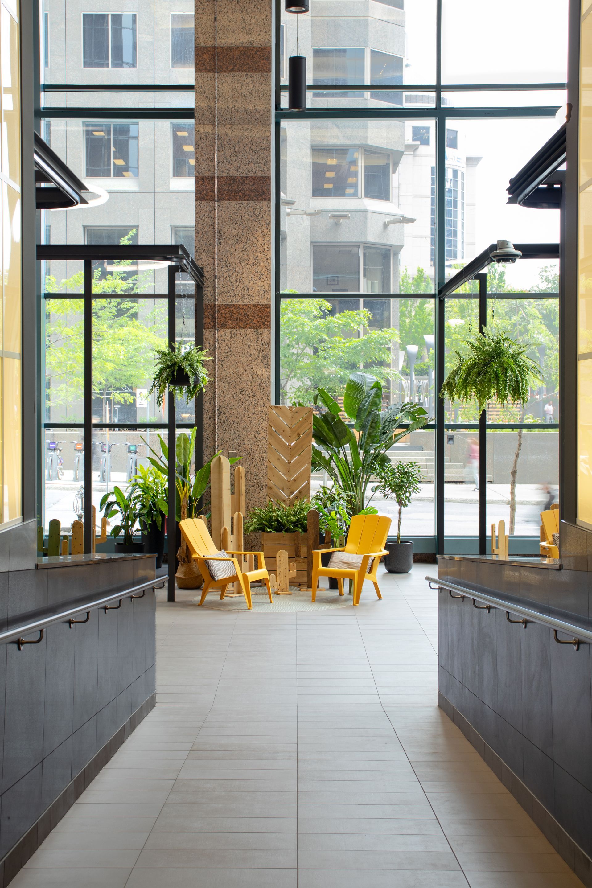 Couloir intérieur avec de grandes fenêtres. Chaises jaunes, plantes et colonne texturée.