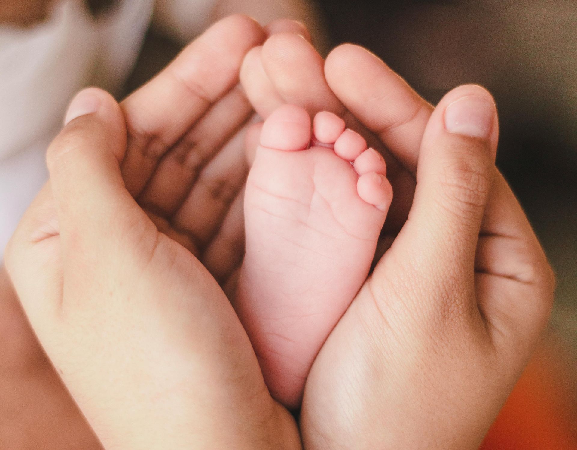 Handjes die een klein babyvoetje vasthouden; roze huid, onscherp.