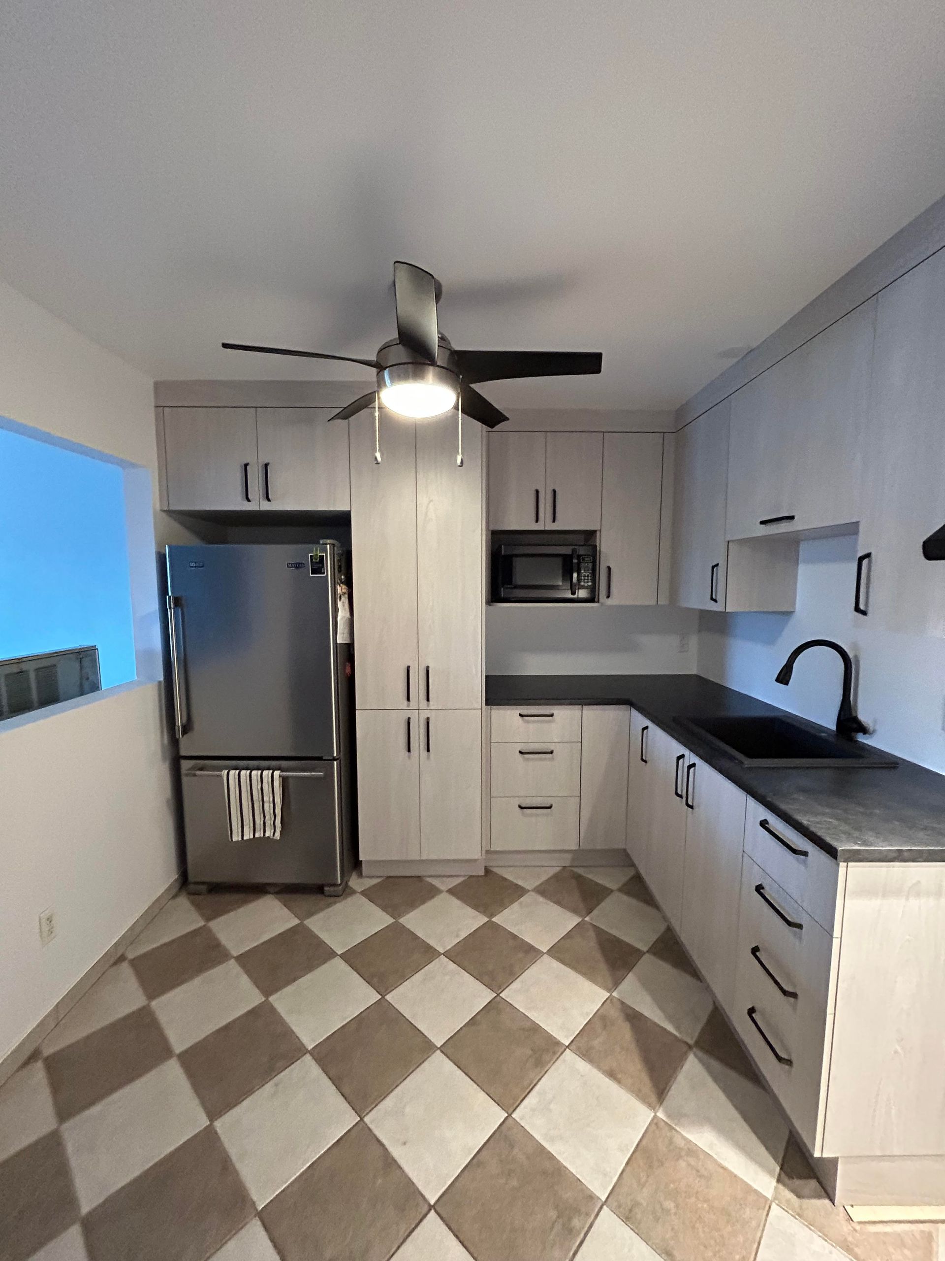 Une cuisine avec un sol en damier et un ventilateur de plafond