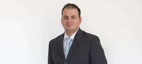 A man in a suit and tie is standing in front of a white wall.