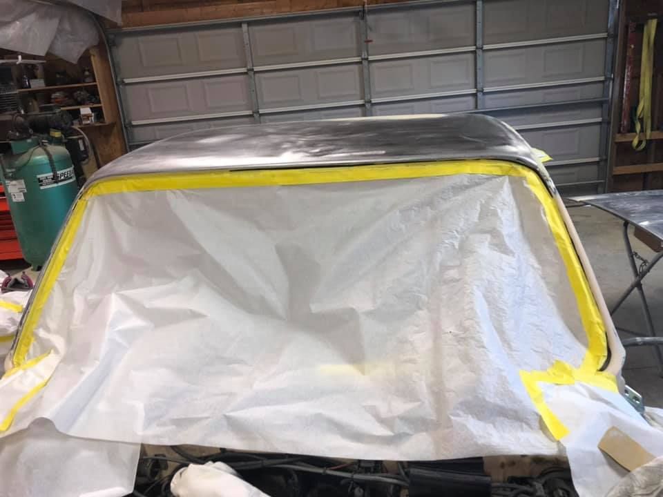 Car covered in white plastic sheeting and yellow painter’s tape inside a garage