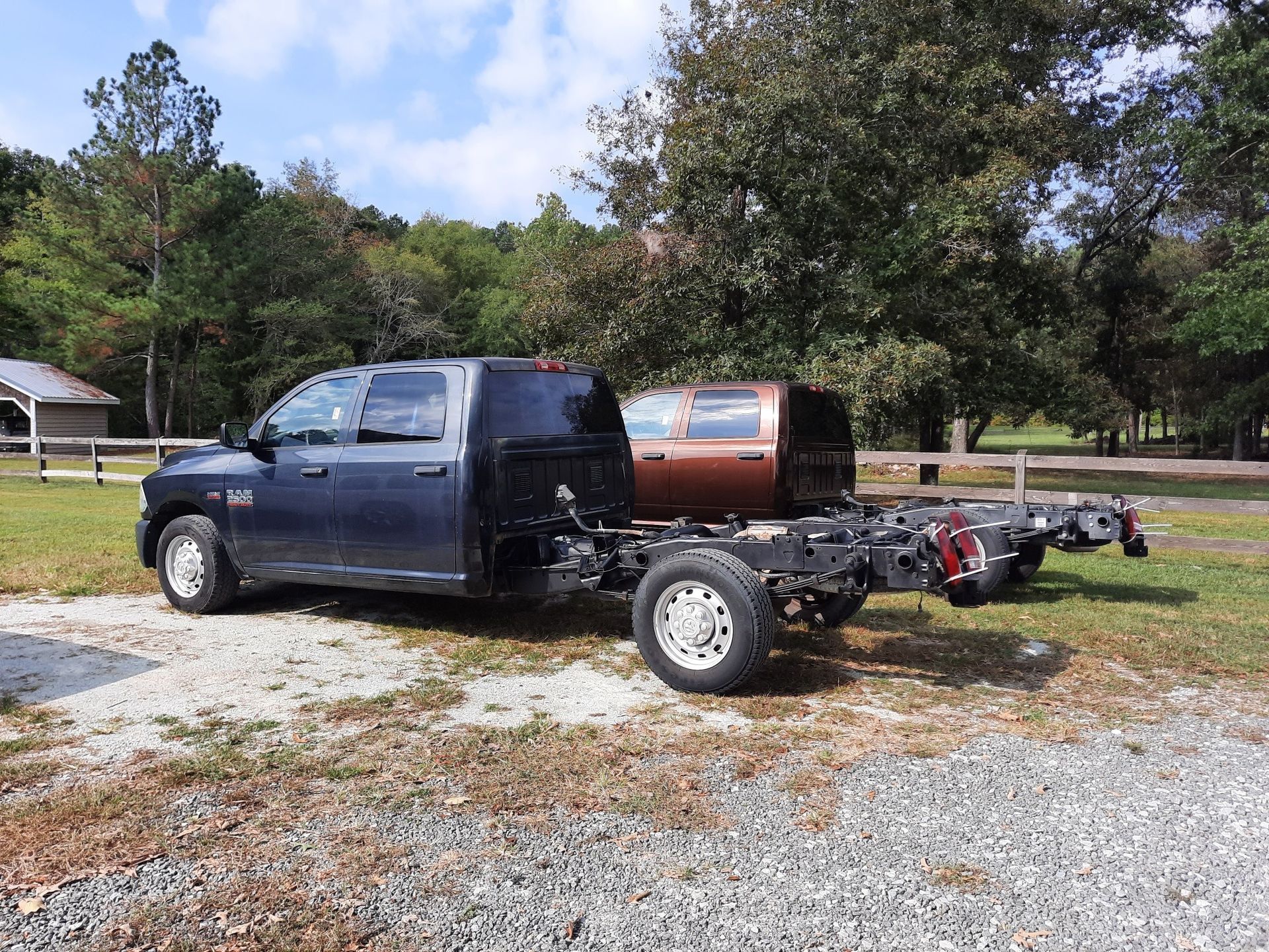 Blue pickup truck chassis with rear body removed, parked on gravel in a grassy yard near trees