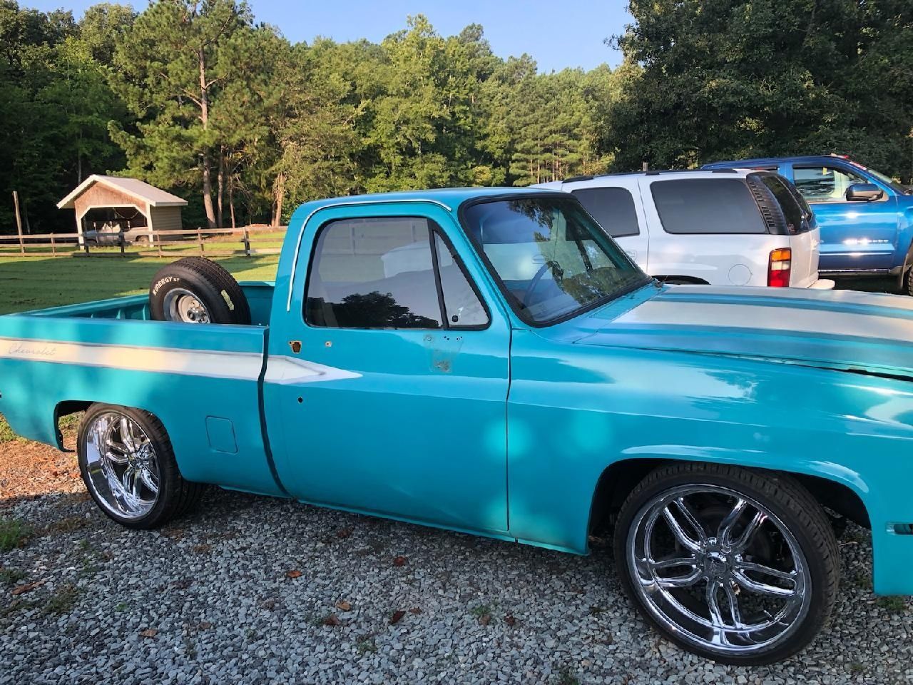 Turquoise vintage pickup truck parked on gravel near other vehicles and trees