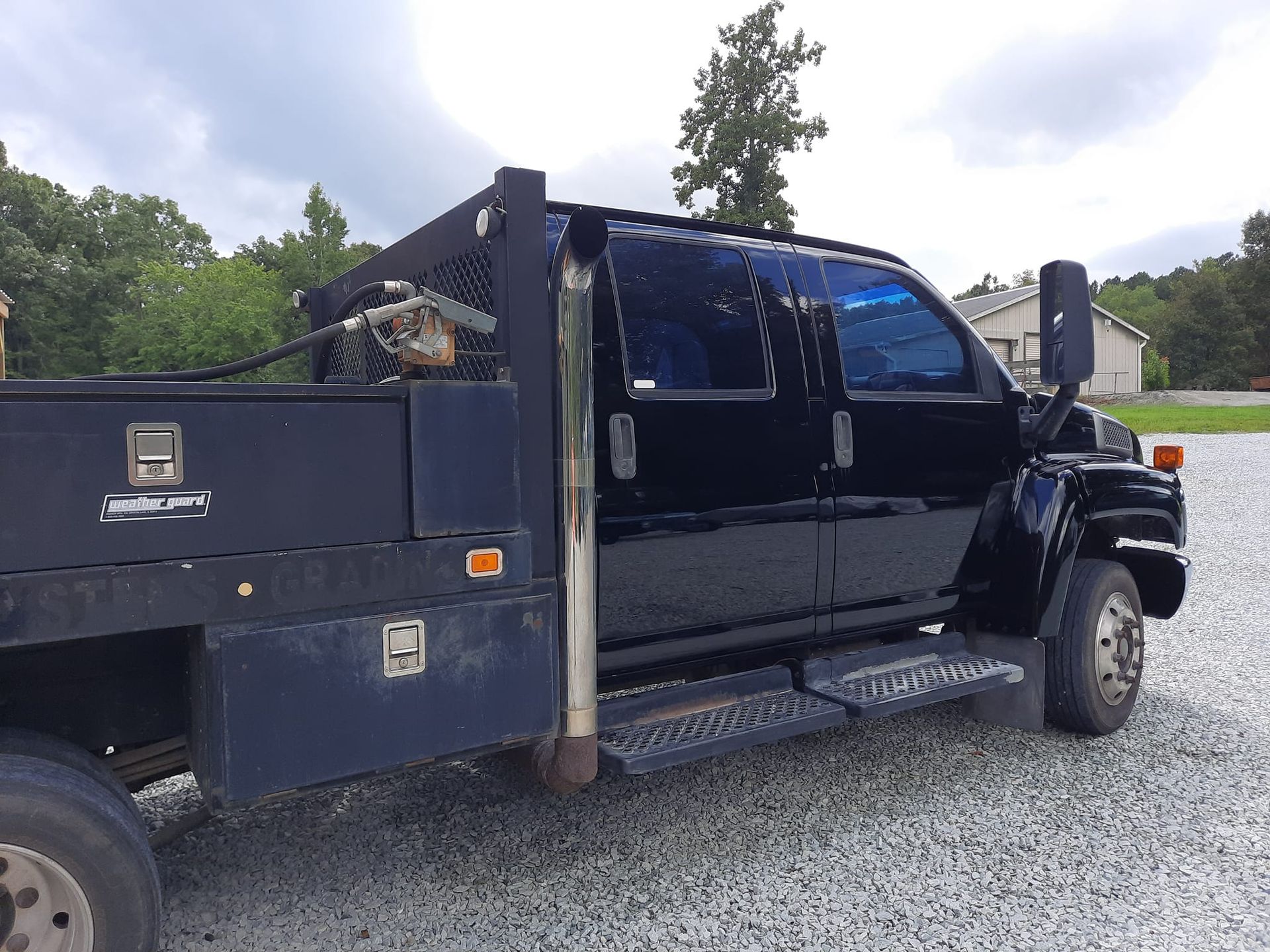 Black dump truck parked on gravel beside trees and a mountain road.