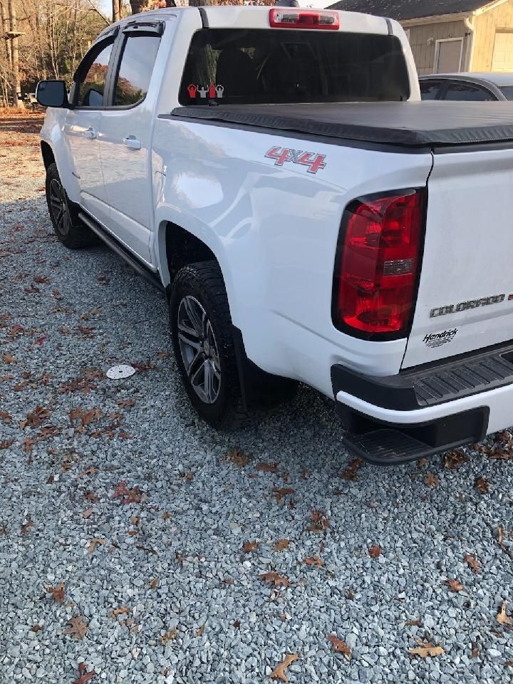 White pickup truck parked on gravel, rear three-quarter view with black tonneau cover.