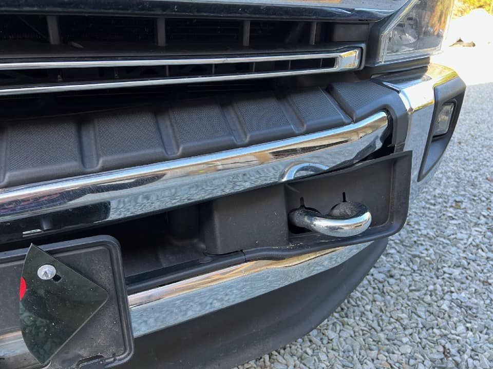 Close-up of a vehicle’s front bumper with a mounted trailer hitch and open electrical connector cover.