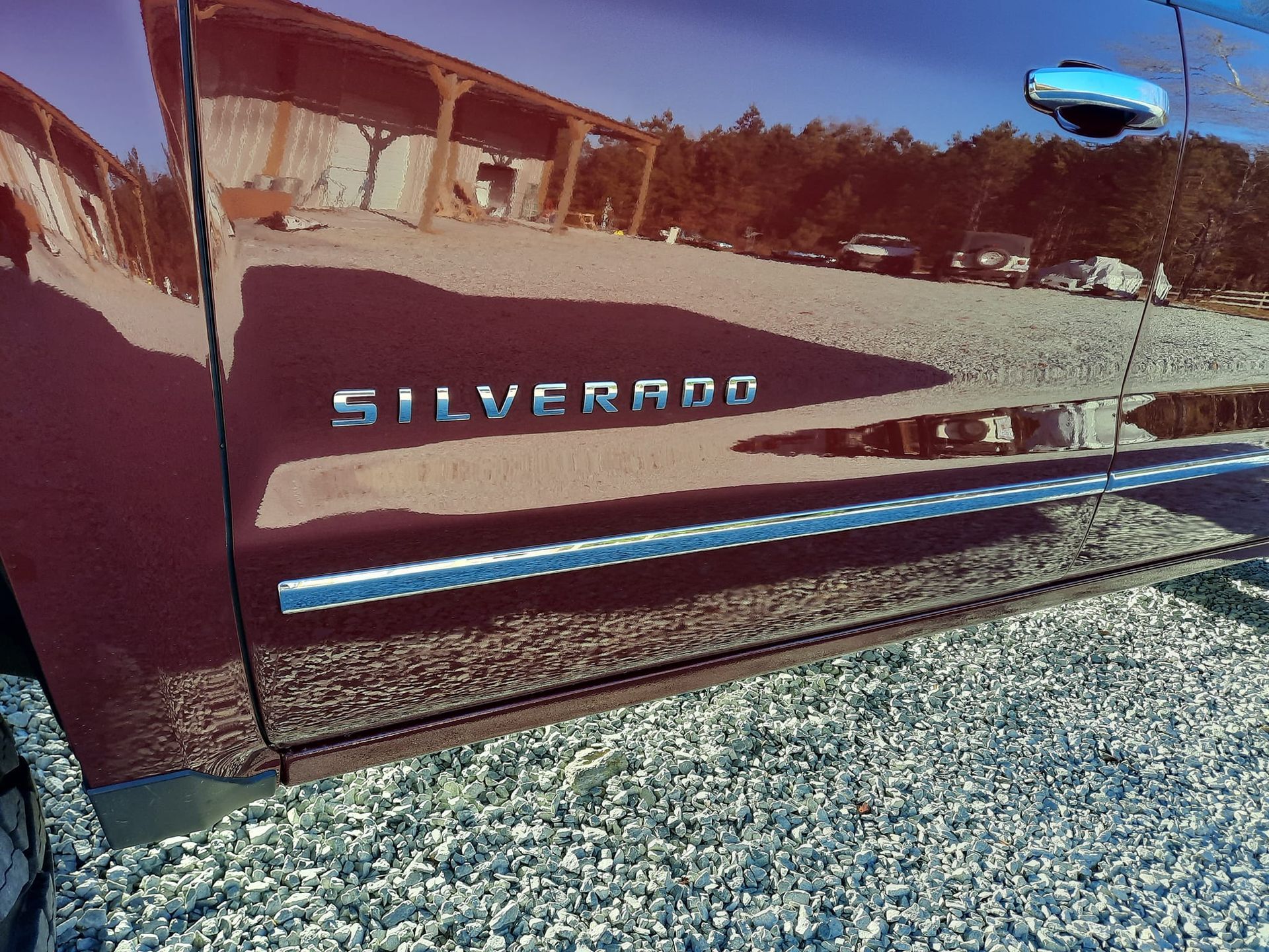 Close-up of a maroon Chevrolet Silverado truck door with chrome trim and emblem.