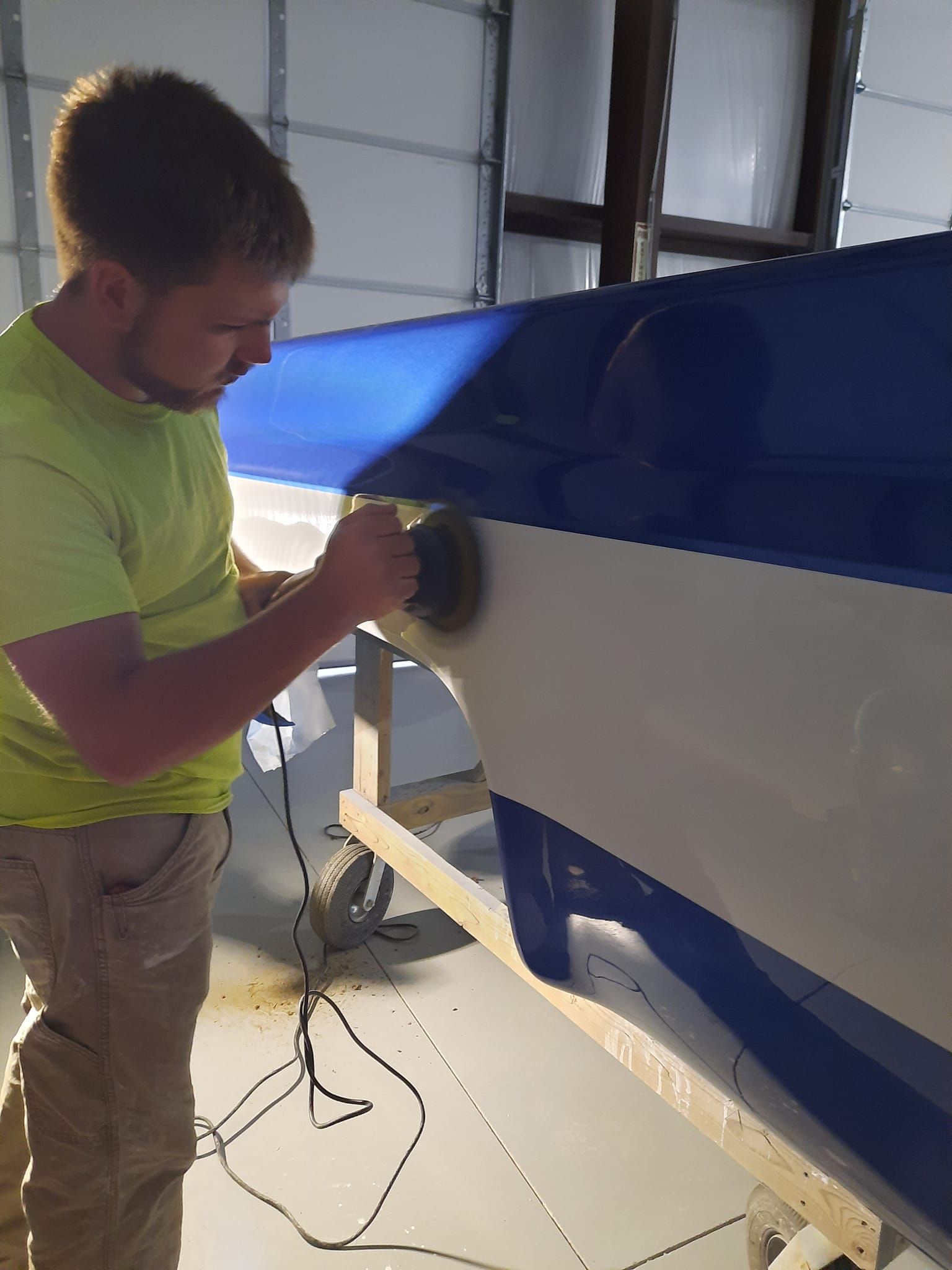 Person sanding a blue-and-white boat hull in a workshop