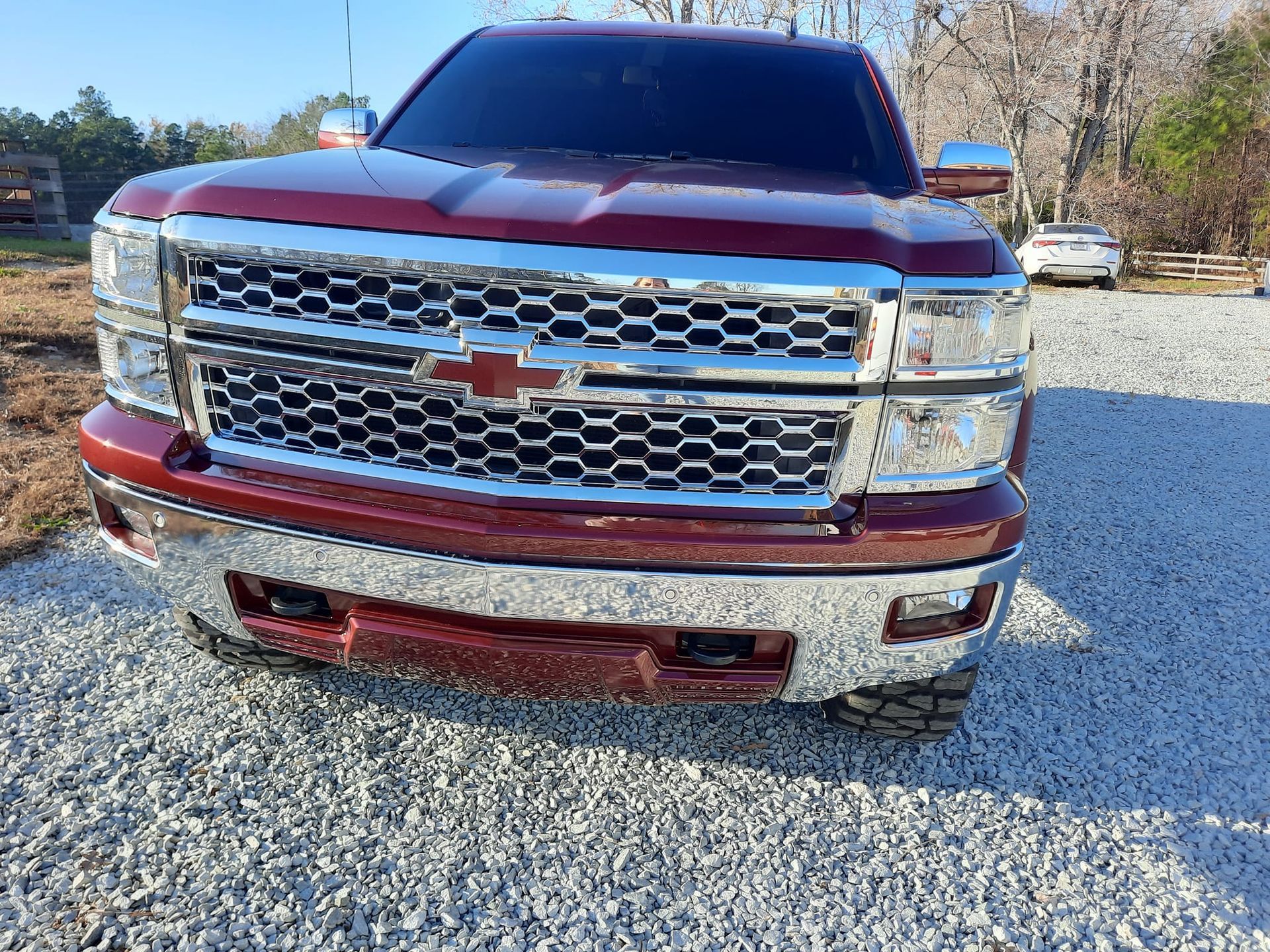 Front view of a maroon Chevrolet pickup truck parked on gravel in bright daylight