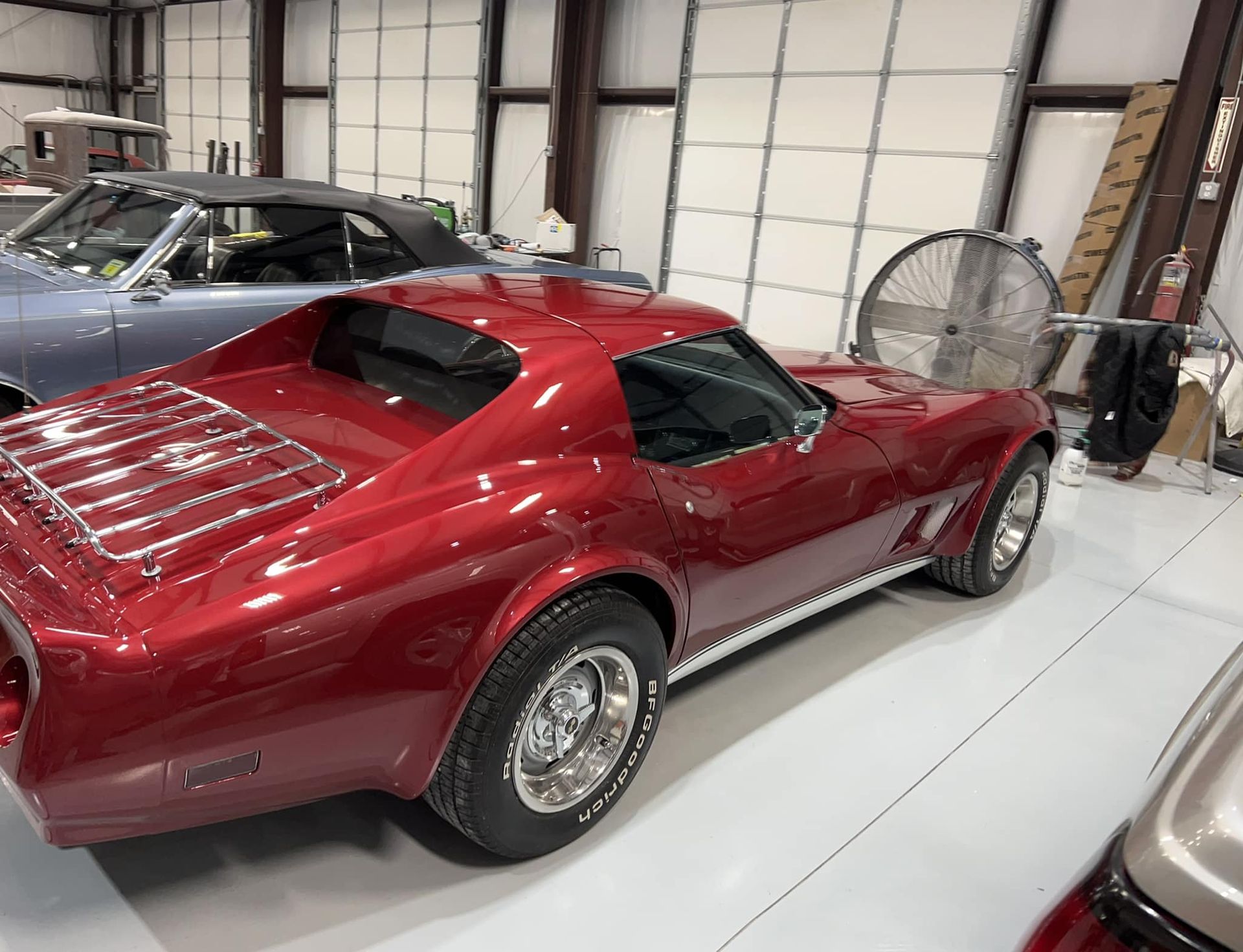 Red classic sports car parked in a garage beside other vehicles