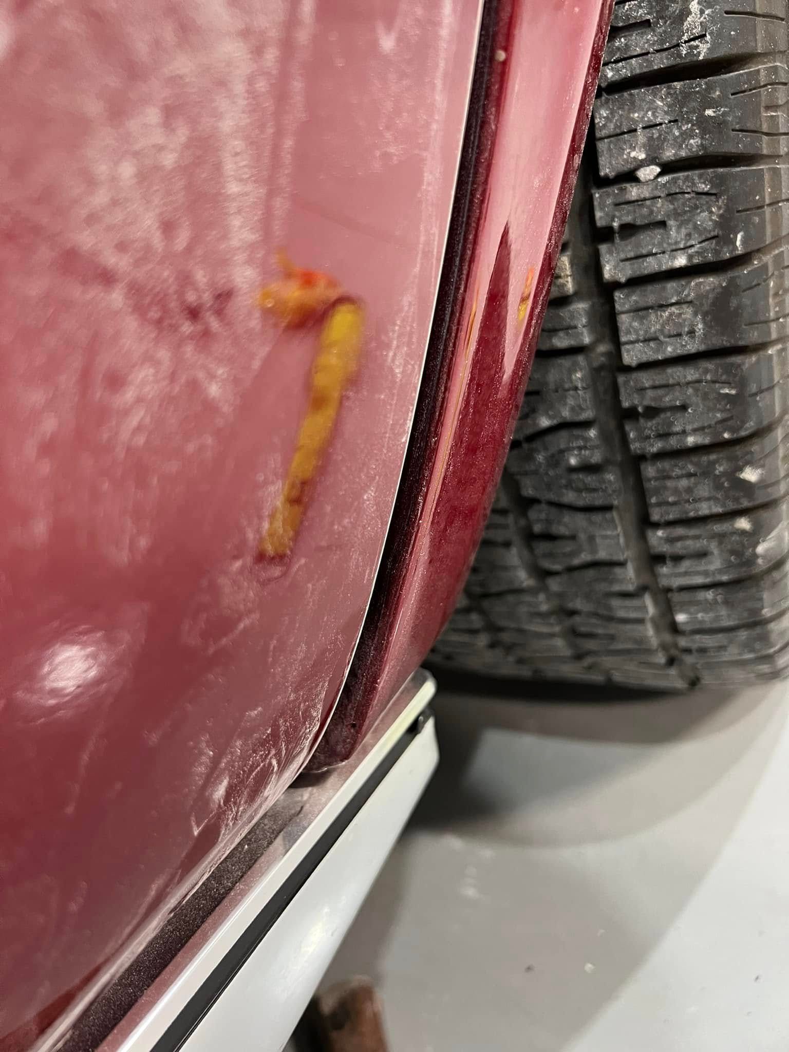 Close-up of a yellow worm on a scratched red car panel beside a tire tread.