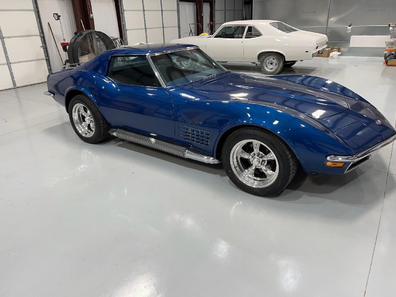 Blue classic sports car in a showroom, with a white vintage car in the background.
