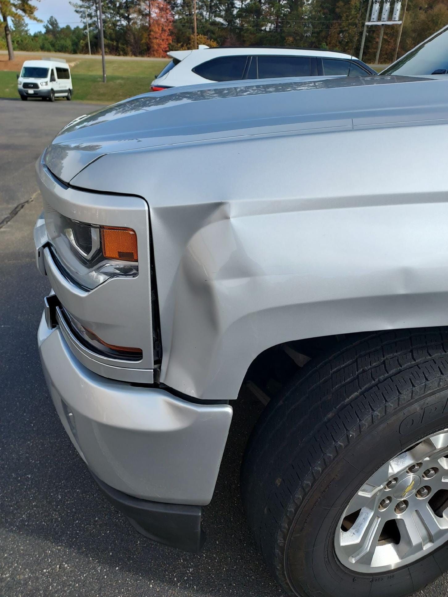 Close-up of a silver pickup truck with a dented front fender and bumper in a parking lot