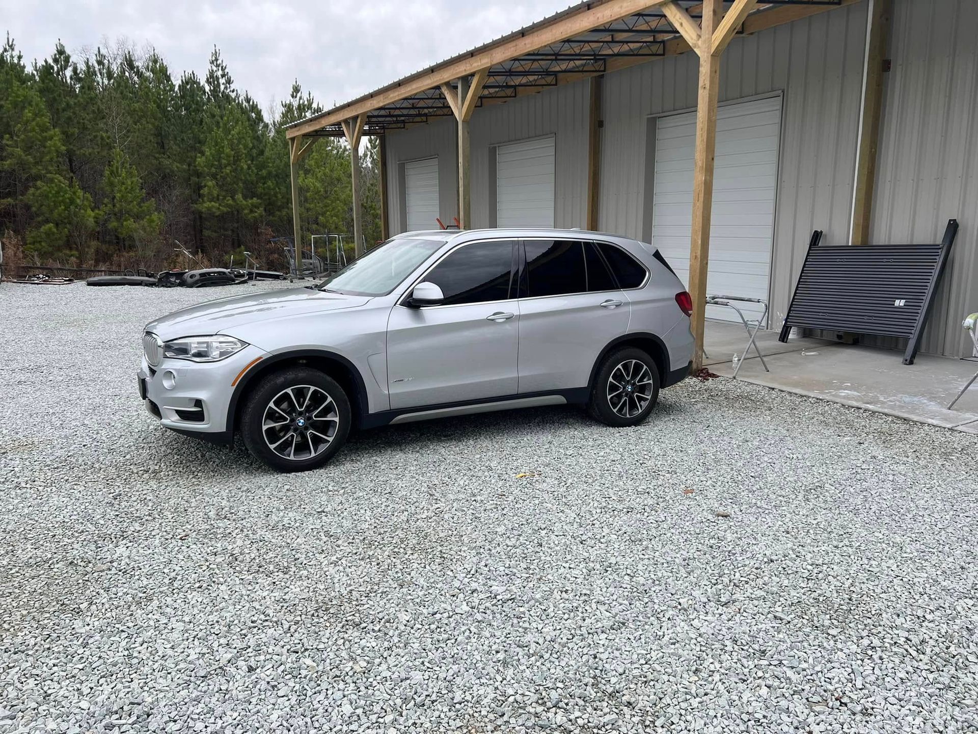 Silver SUV parked on gravel beside a wooden building with a covered porch.