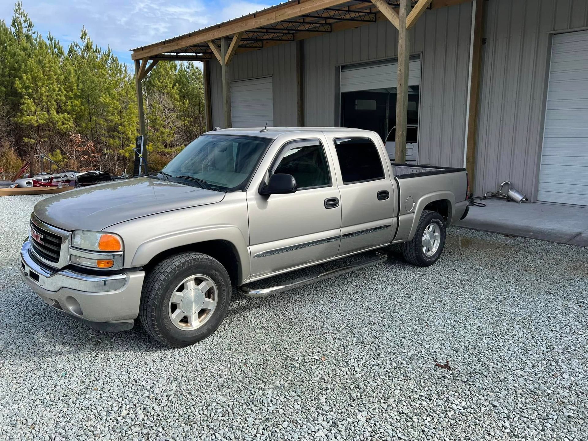 Silver pickup truck parked beside a warehouse on gravel.