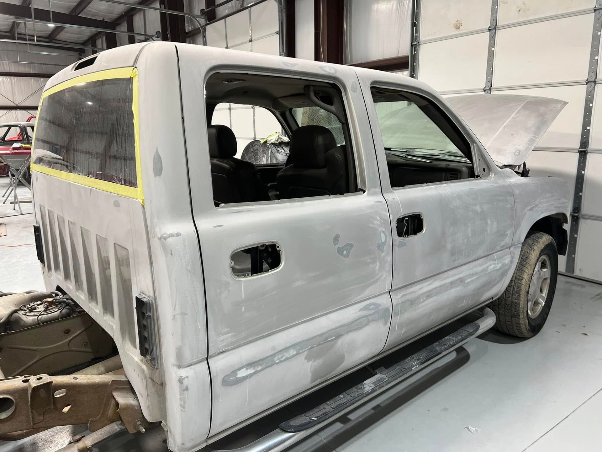 White pickup truck cab in a body shop, with missing front end and window openings taped off