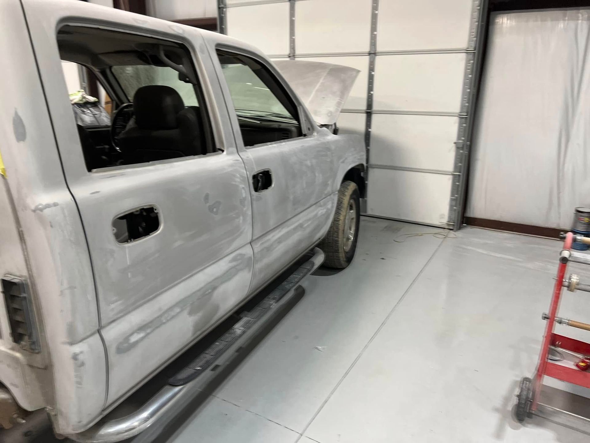 White SUV under repair in a garage, with primer spots and missing trim on the driver’s side.