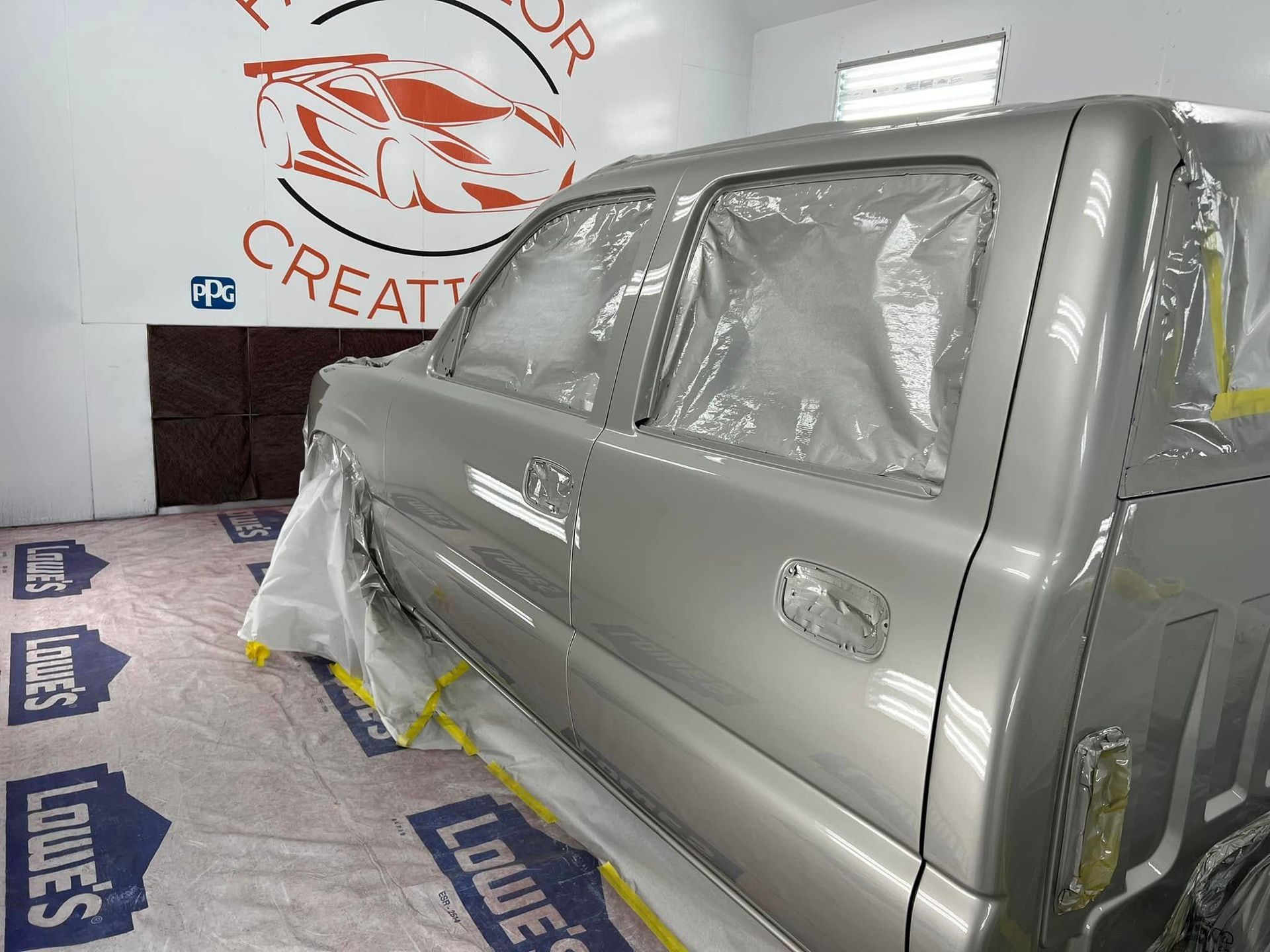 Car wrapped in gray protective film inside a body shop, surrounded by masking materials.