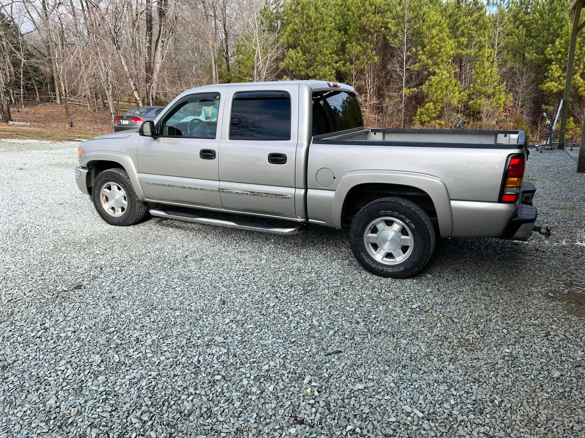 Silver pickup truck parked on gravel in a wooded area with trees in the background