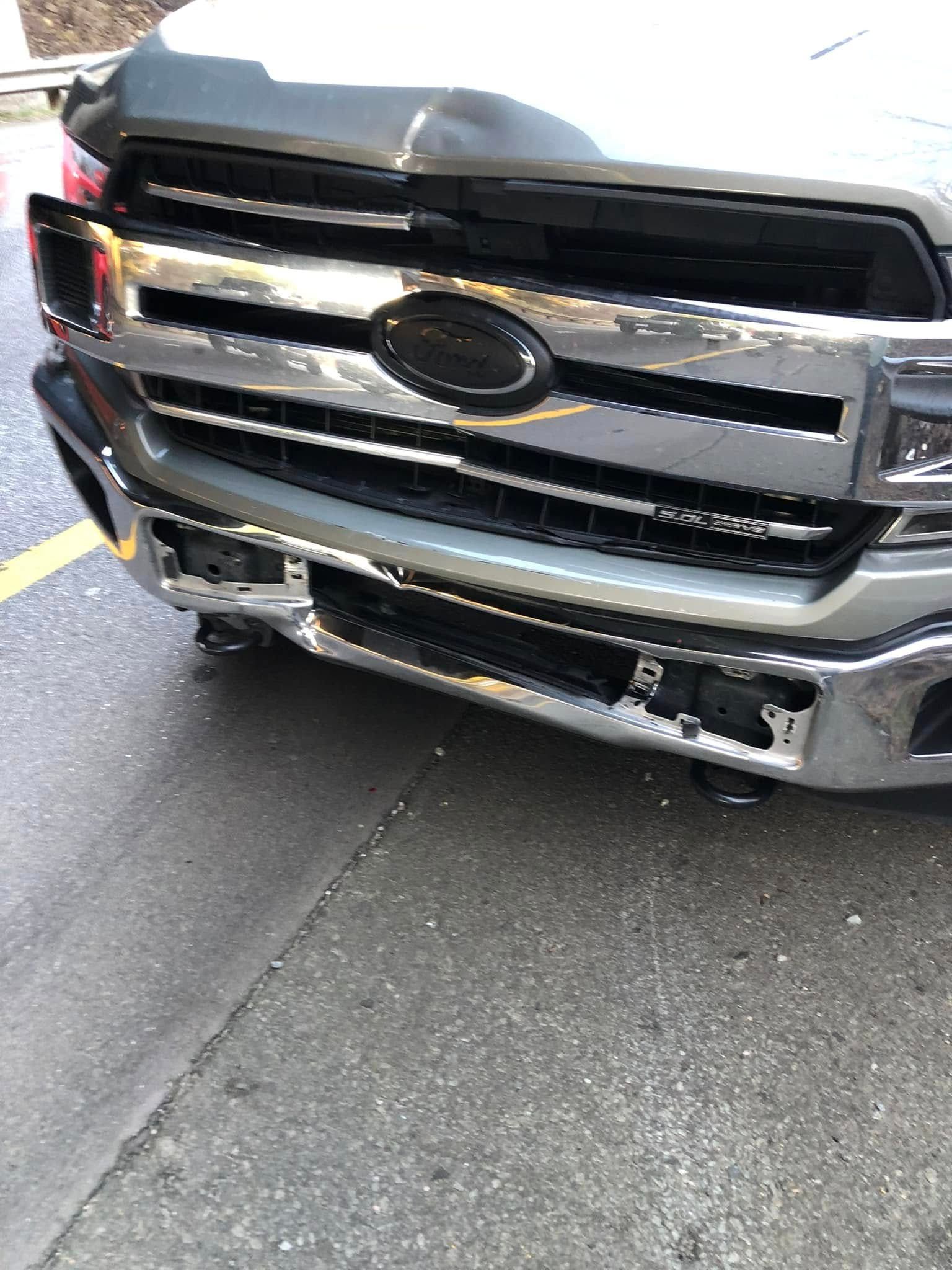 Front view of a black pickup truck with a damaged chrome grille and bumper on pavement