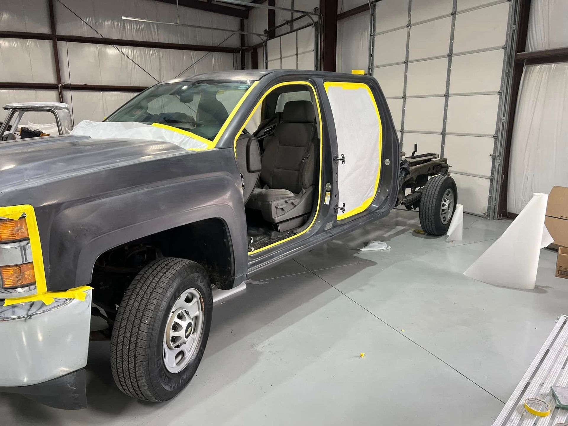 Partially assembled black pickup truck in a workshop, with yellow masking and an open door and cab.