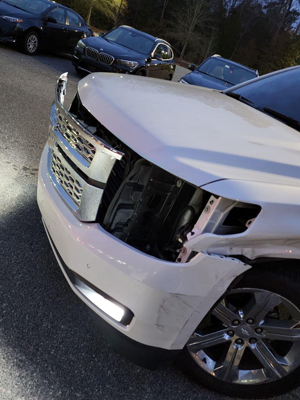 White SUV with front end damage and a missing headlight, parked in a lot.
