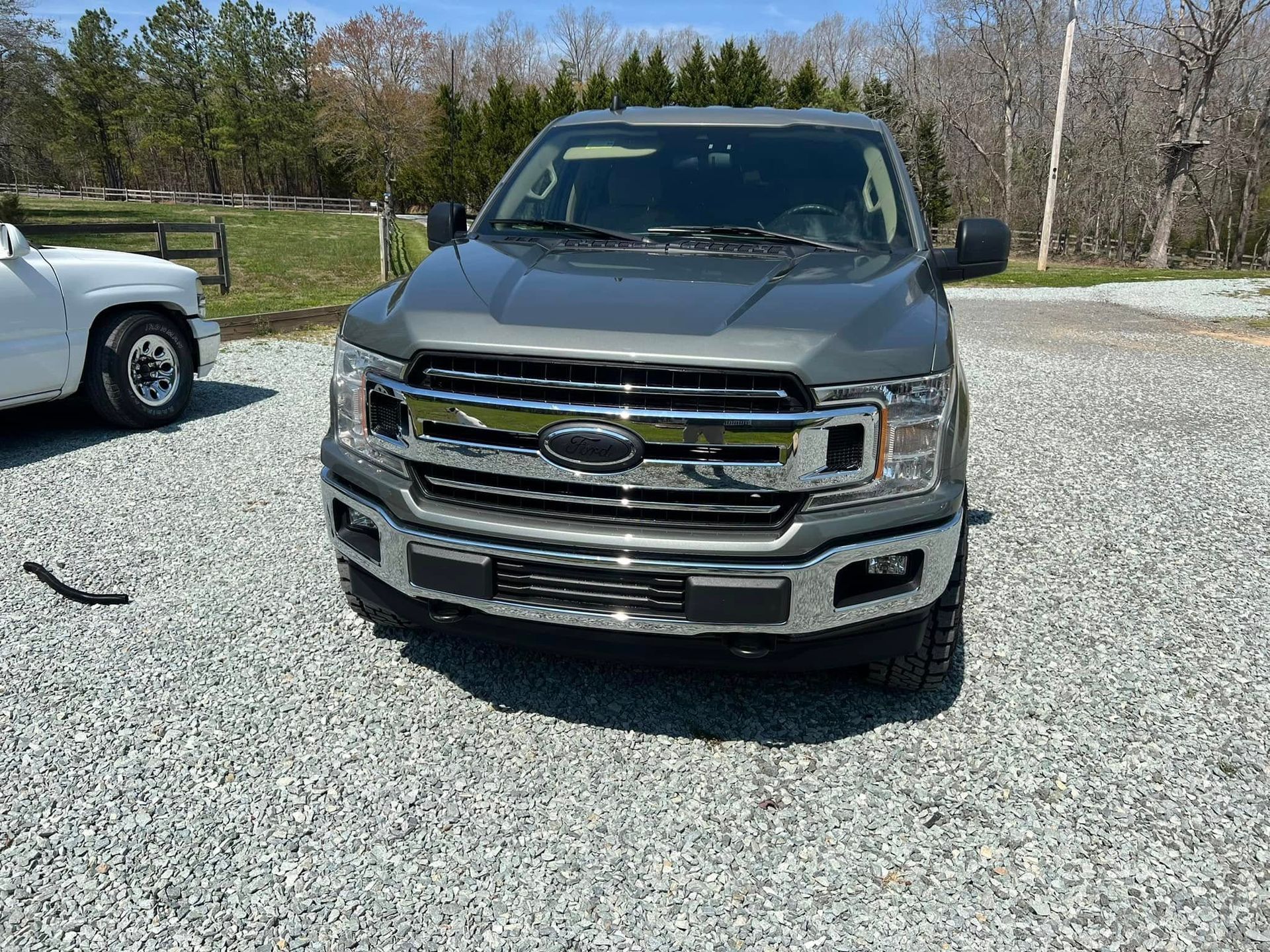 Dark Ford pickup truck parked on gravel lot, front view under a sunny sky