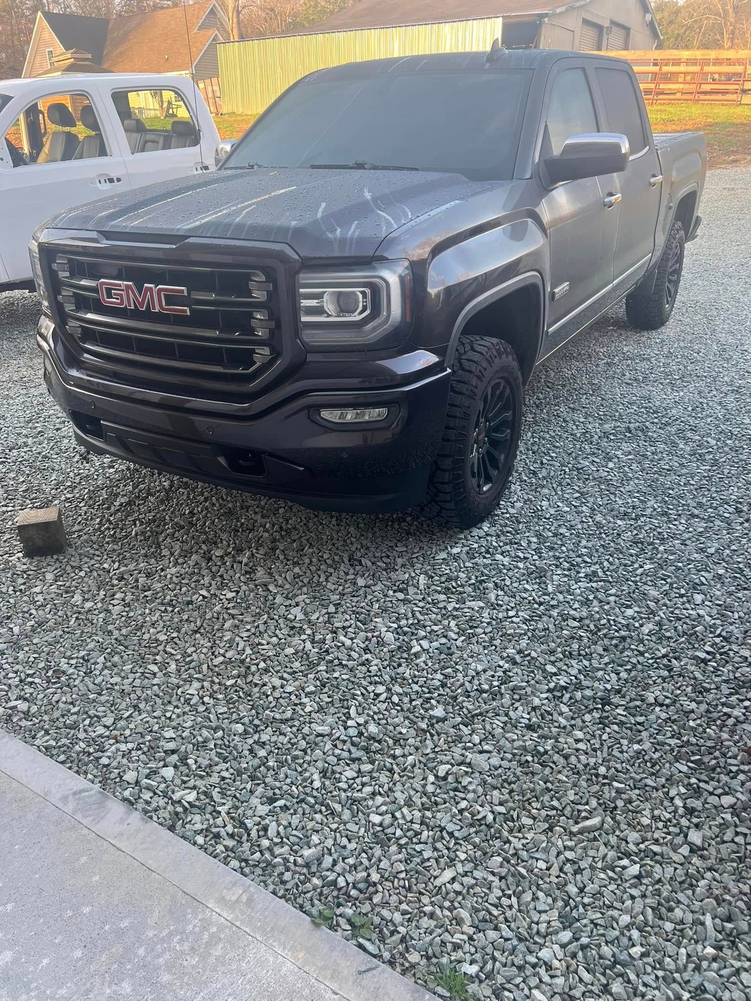 Black GMC pickup truck parked on gravel beside a yellow vehicle outdoors