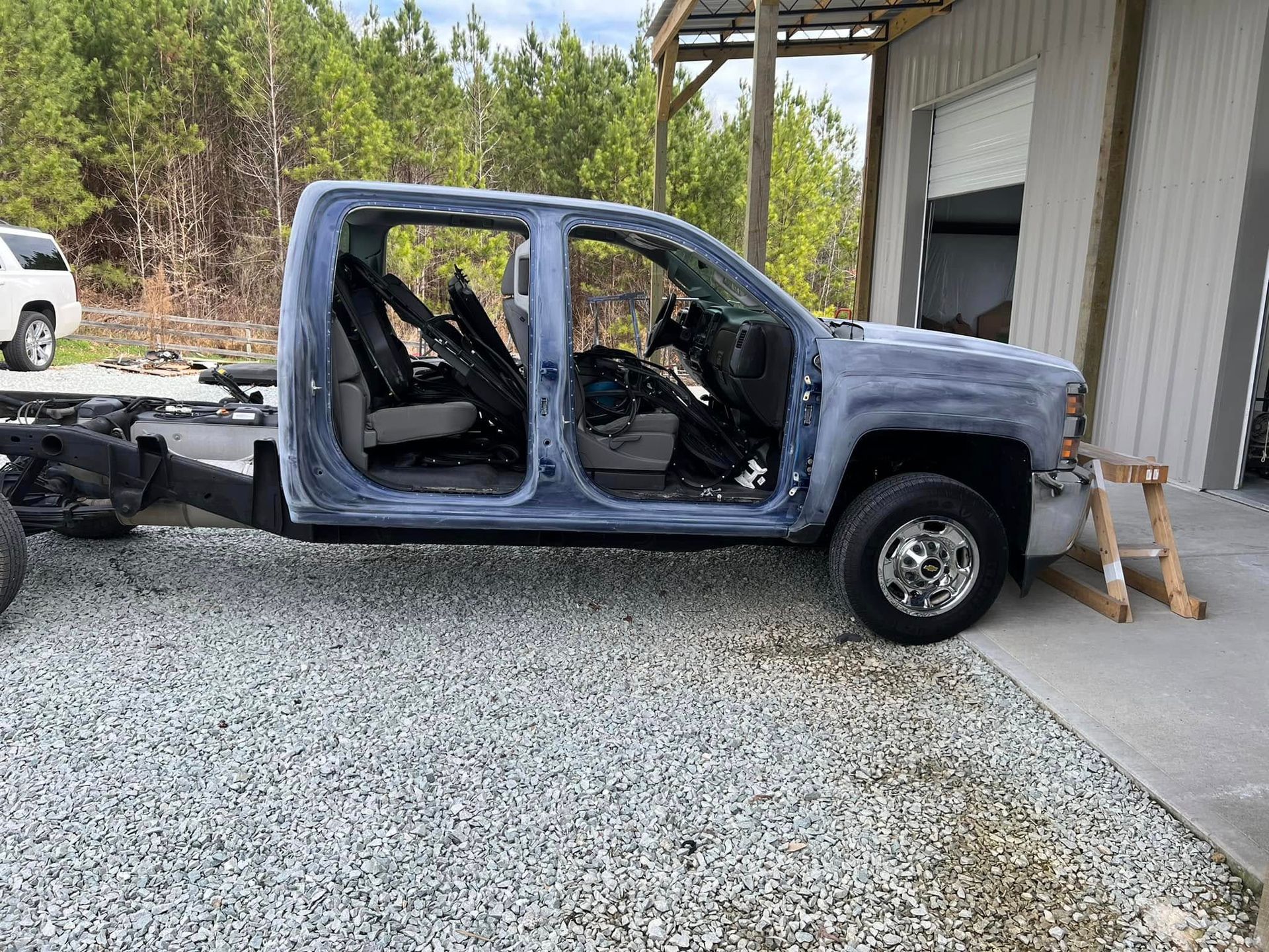 Blue-gray pickup truck without doors parked beside a building on a gravel drive