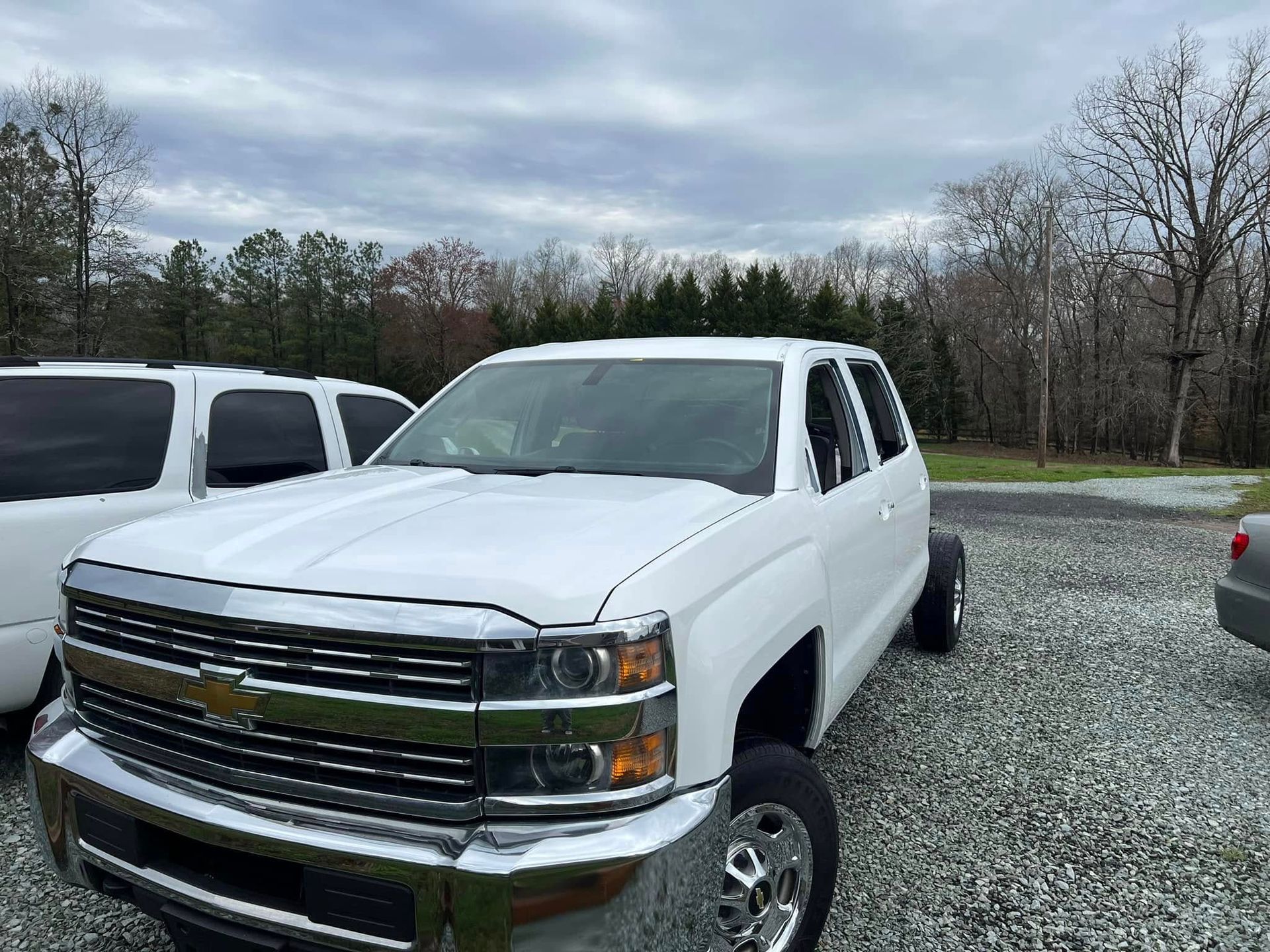 White Chevrolet pickup truck parked on gravel lot under cloudy sky, with other vehicles nearby