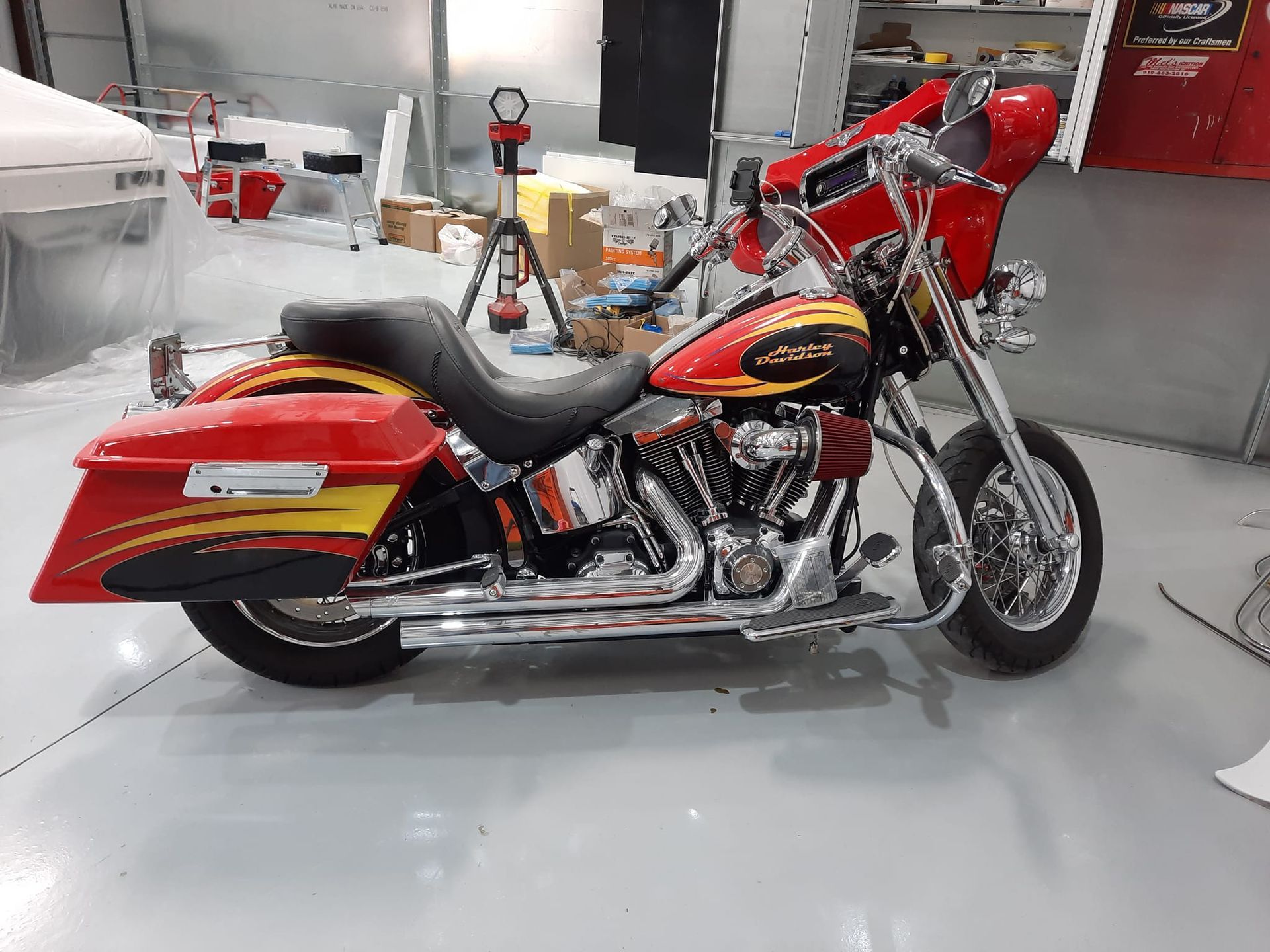 Red and black custom Harley-Davidson motorcycle in a workshop, viewed from the side.