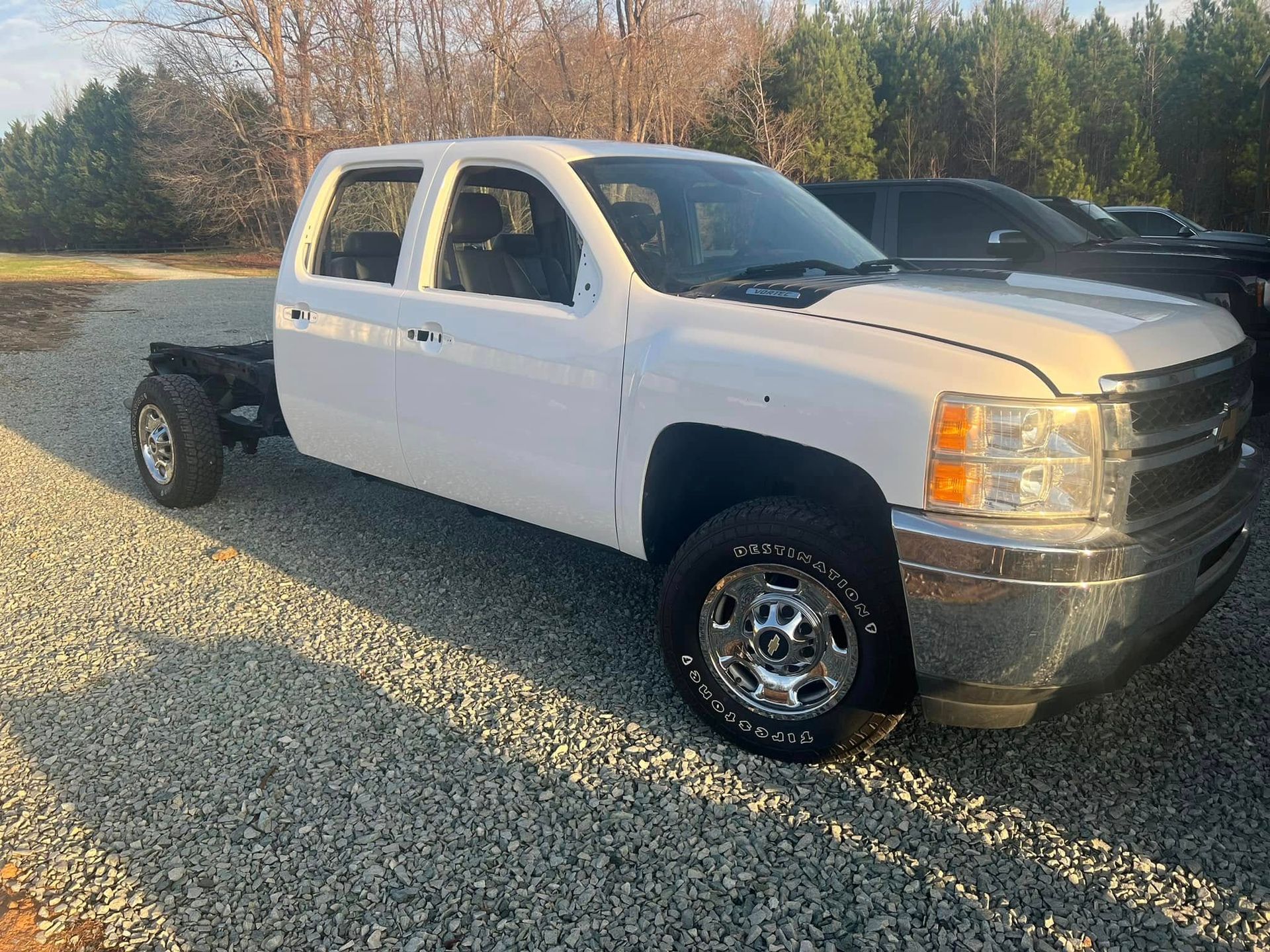 White extended-cab pickup truck with flatbed frame parked on gravel in daylight