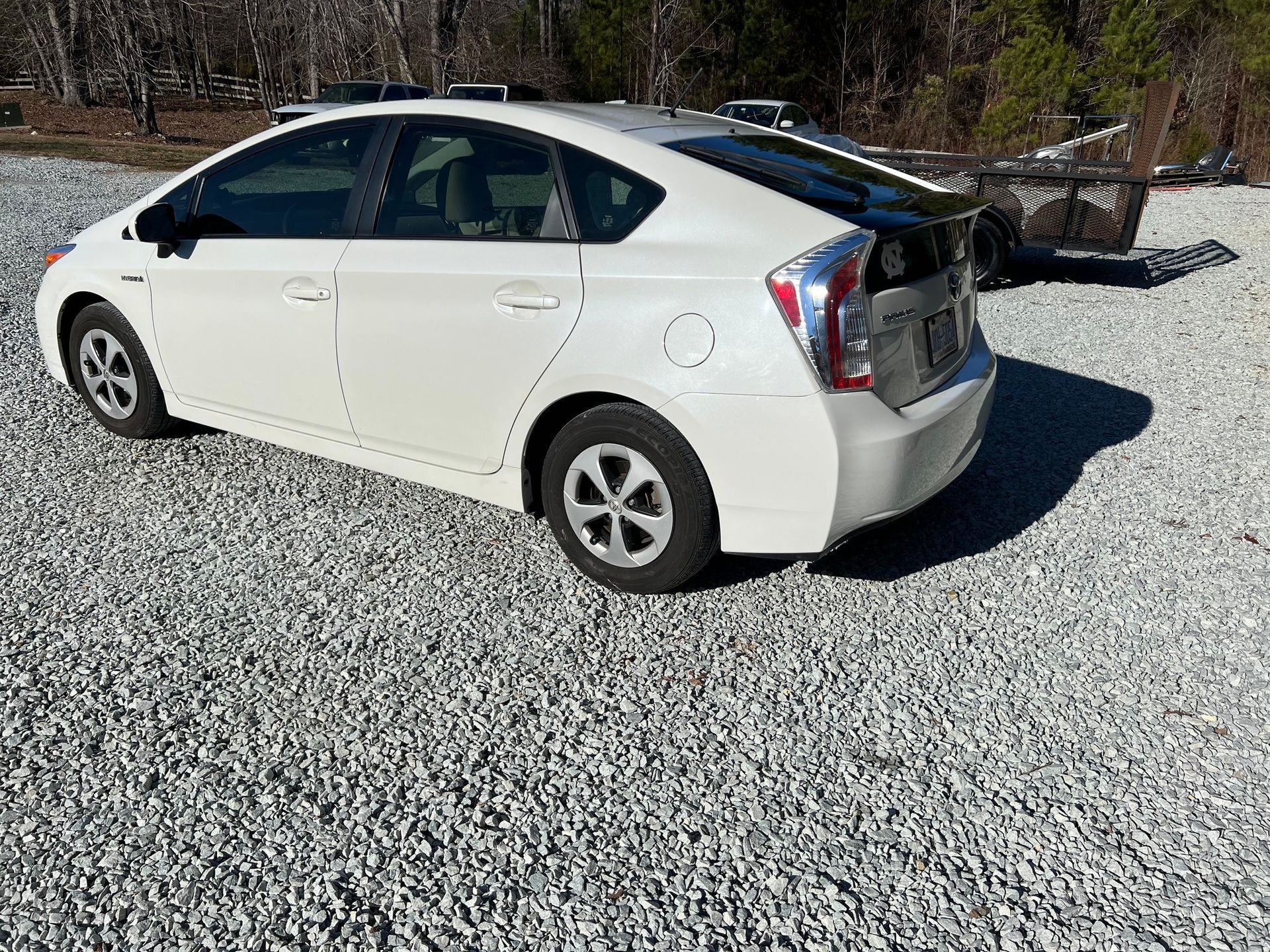 White Toyota Prius parked on gravel driveway beside trees, rear hatch open