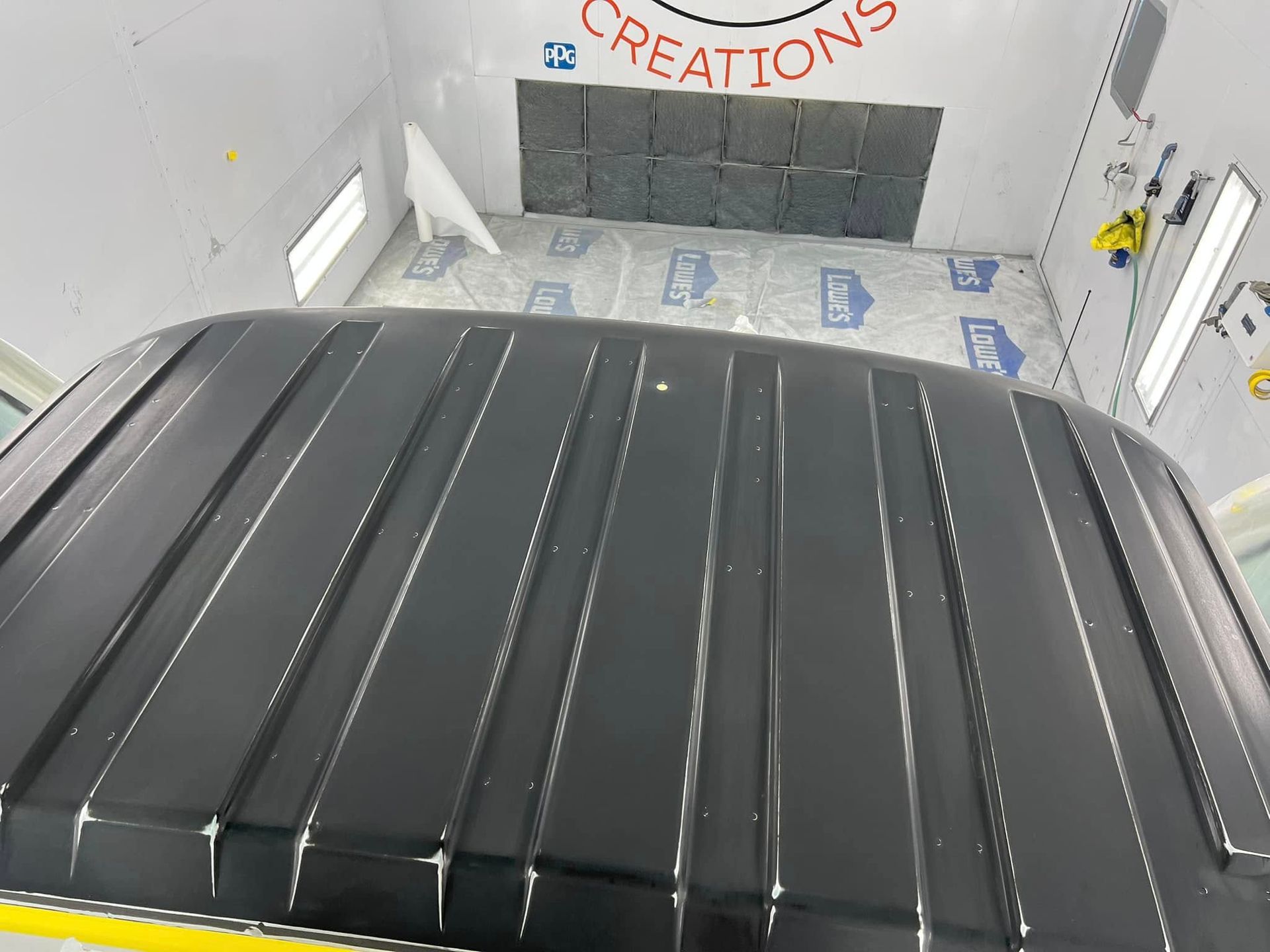 Black truck roof in an auto body paint booth with “Creations” on the back wall