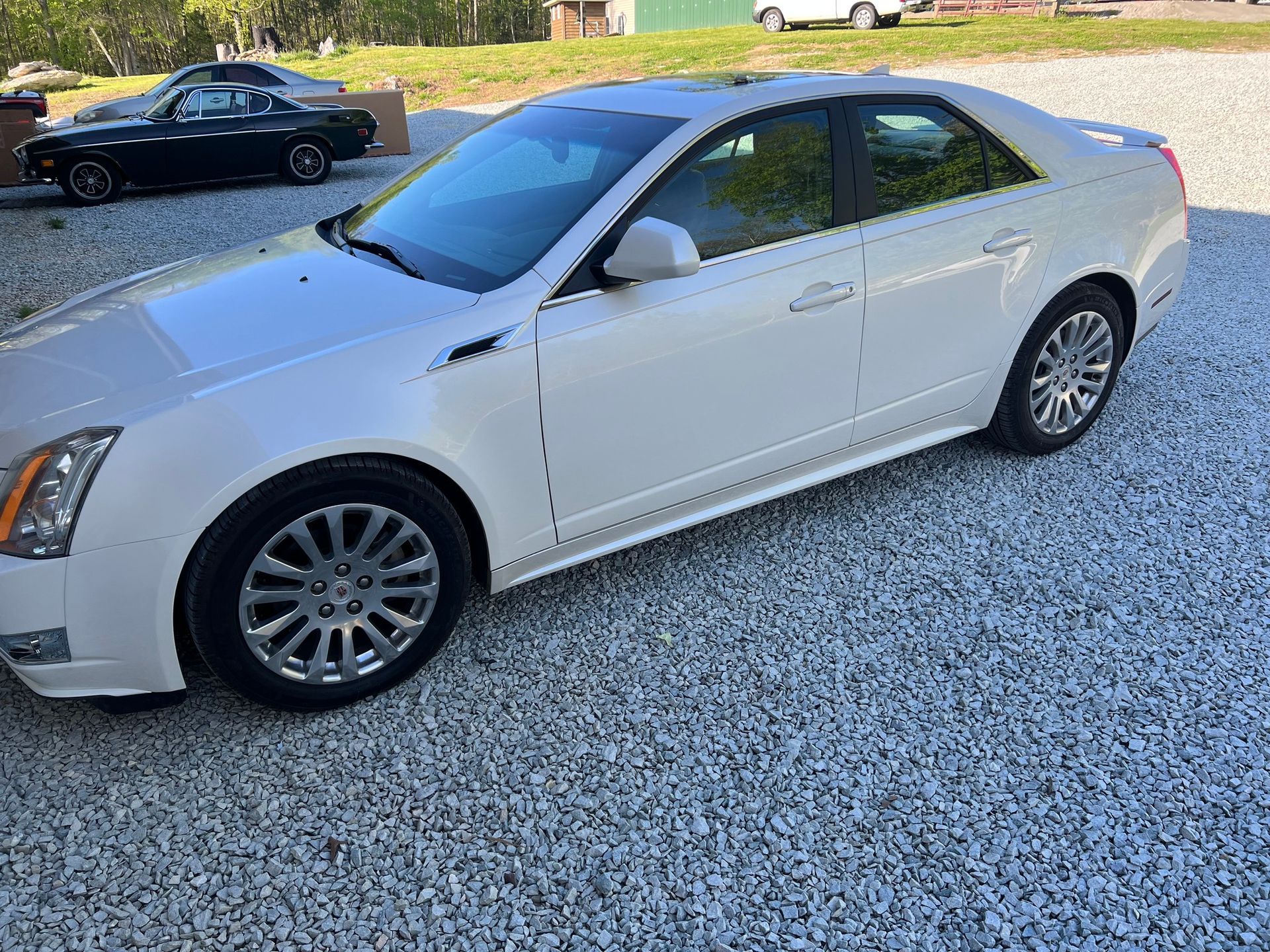 Silver sedan parked on a gravel driveway with a black car in the background.