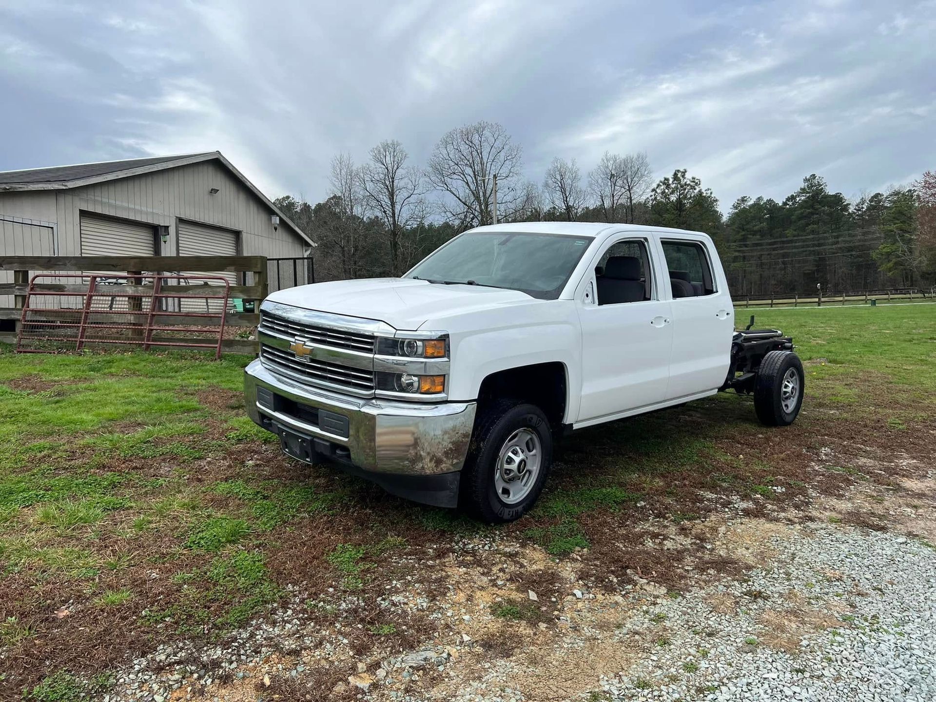 White pickup truck parked on a gravel lot beside a barn under an overcast sky
