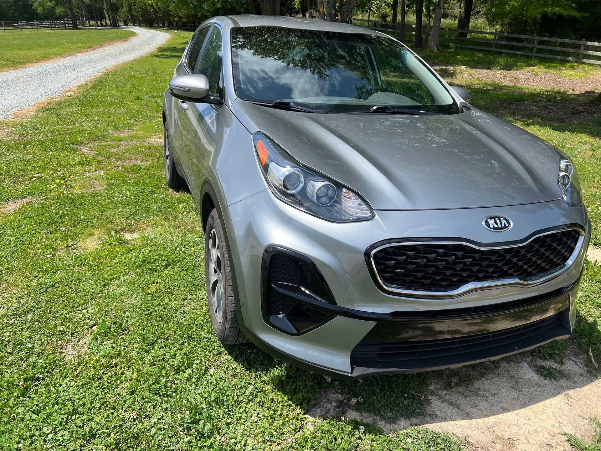 Silver SUV parked on grass beside a gravel path in a sunny park-like setting