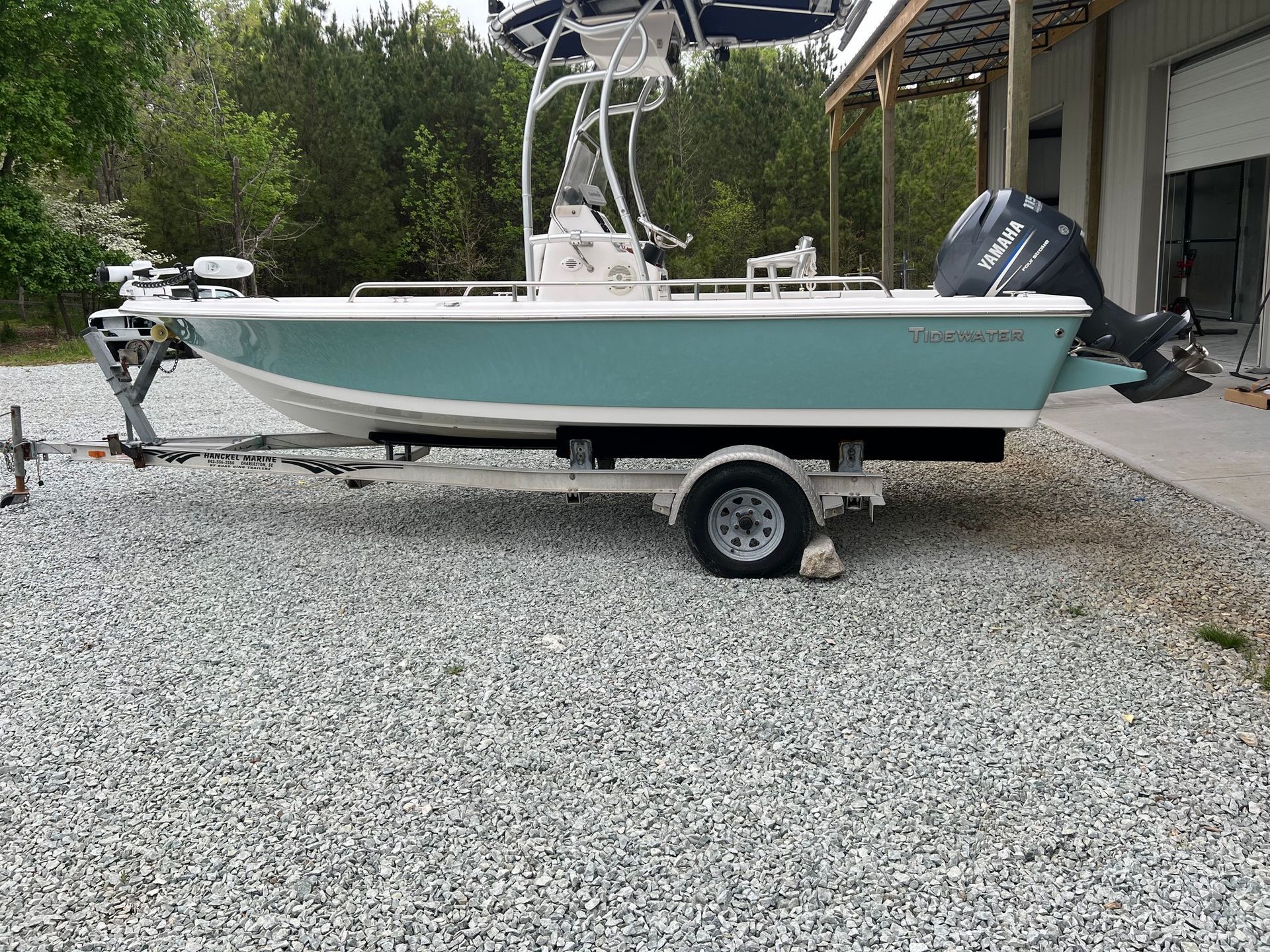 Mint green boat on a trailer parked on gravel beside a driveway.