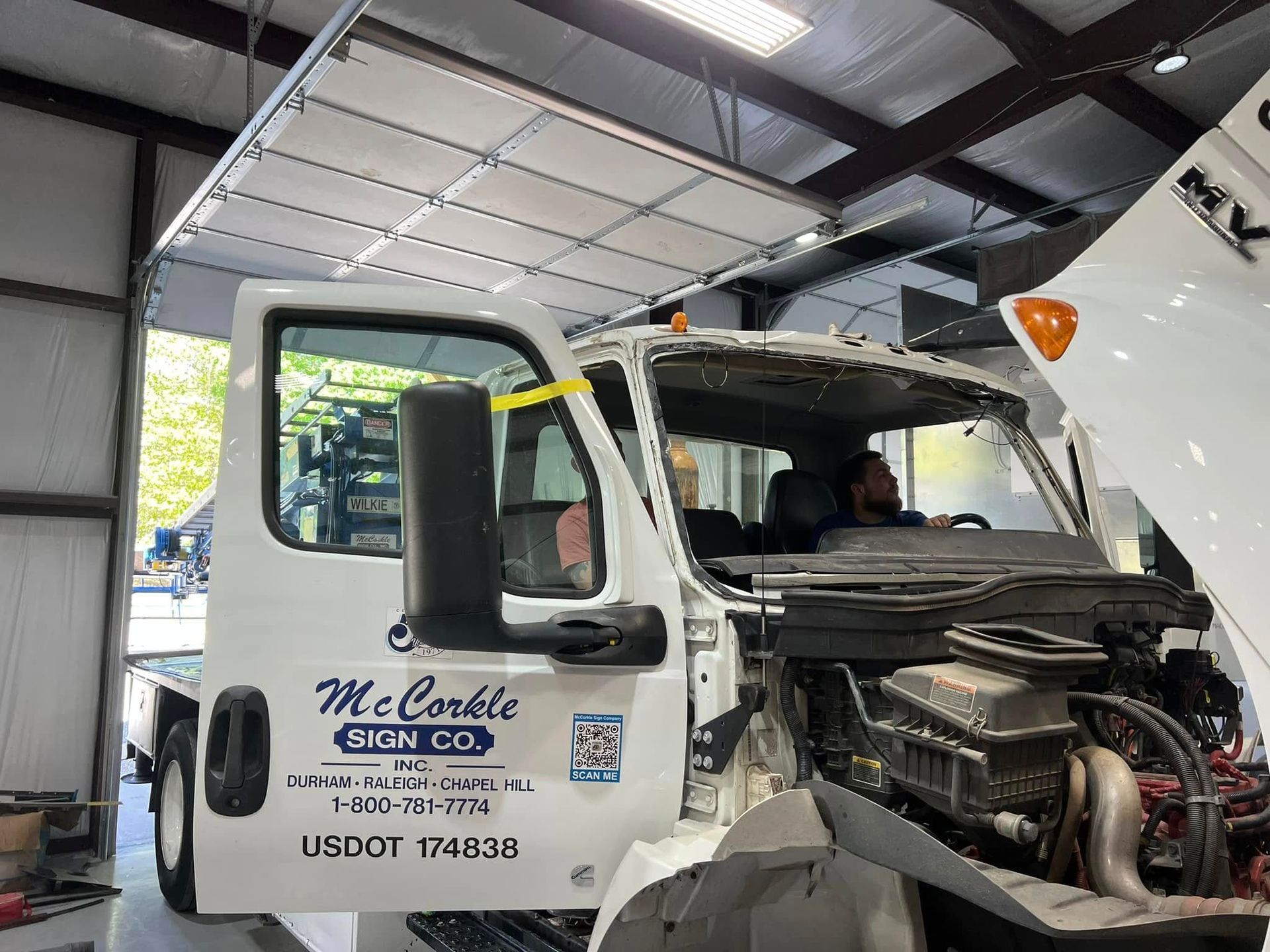 Damaged white tow truck inside a garage, front end exposed and hood open