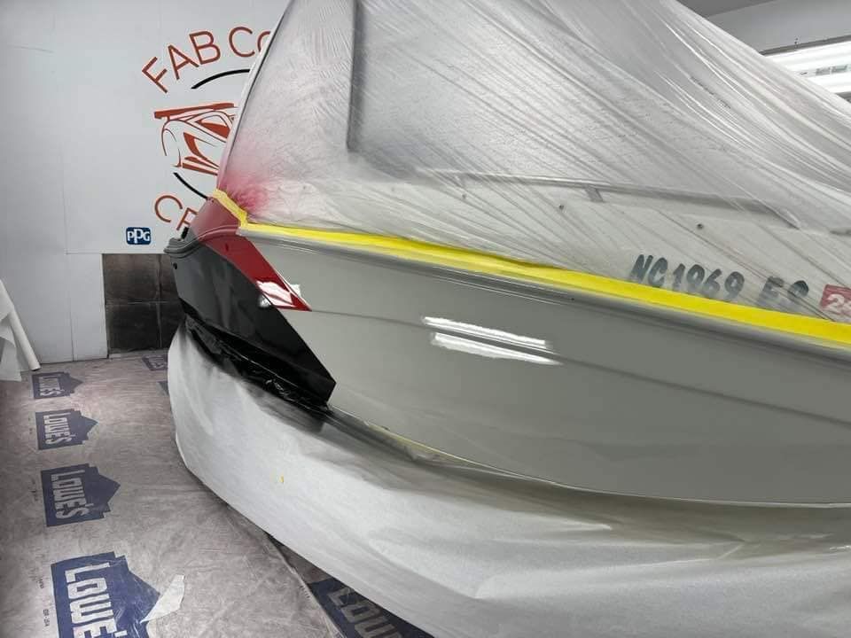 Large boat wrapped in white protective plastic in a garage, with black and red trim visible.