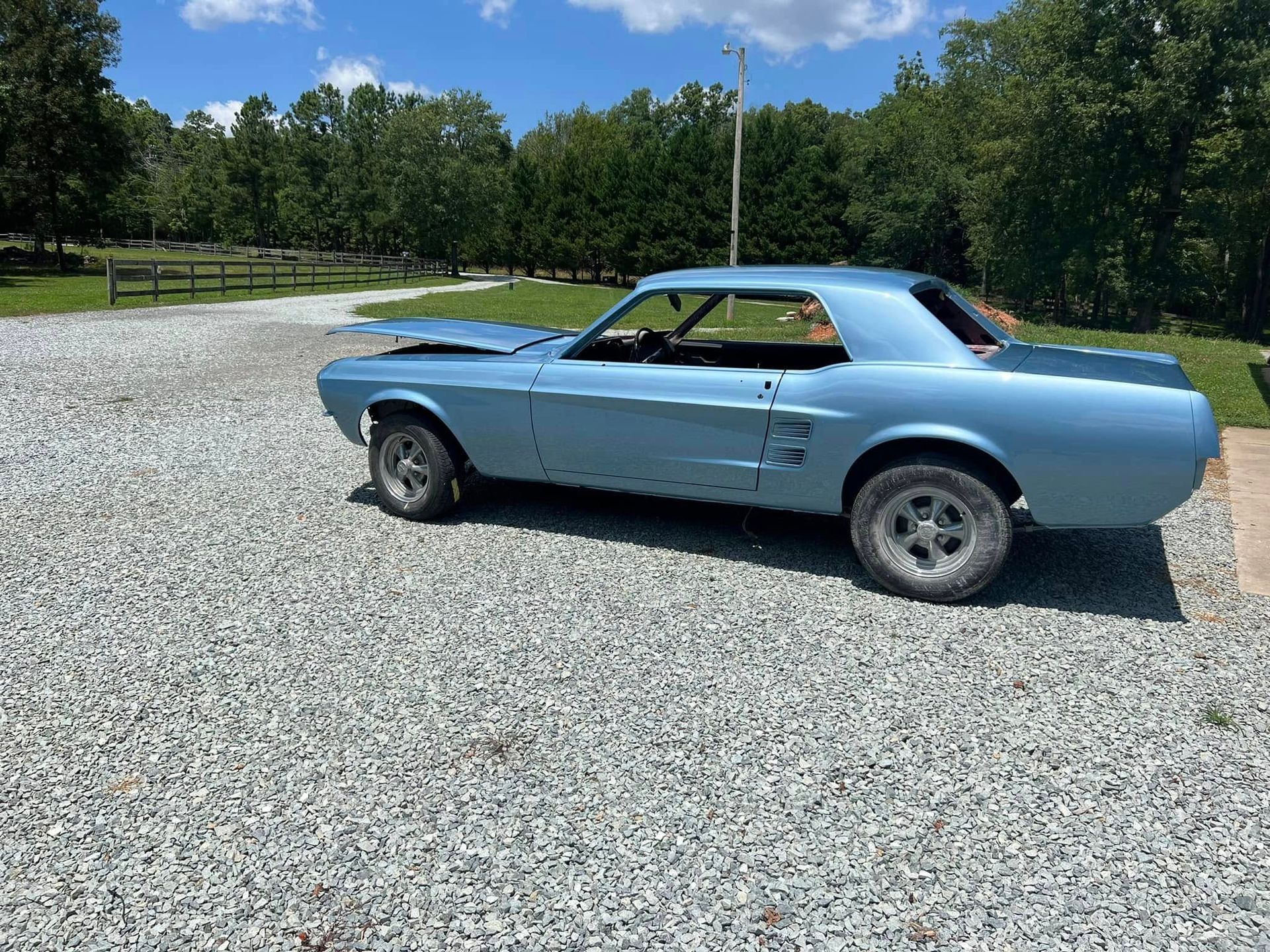 Light blue classic muscle car parked on a gravel lot under a blue sky