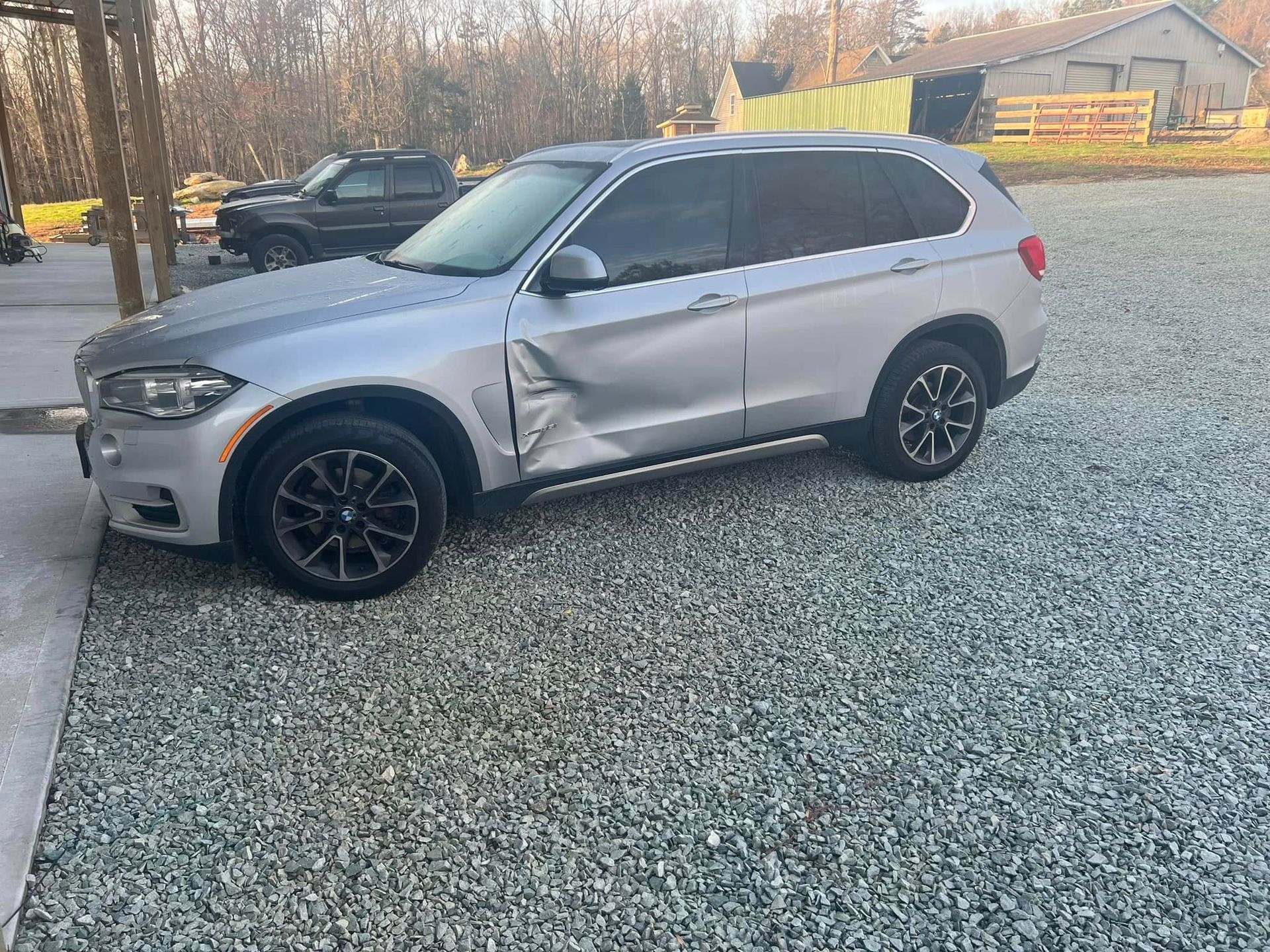 Silver SUV with damaged driver-side door, parked on gravel in a driveway.
