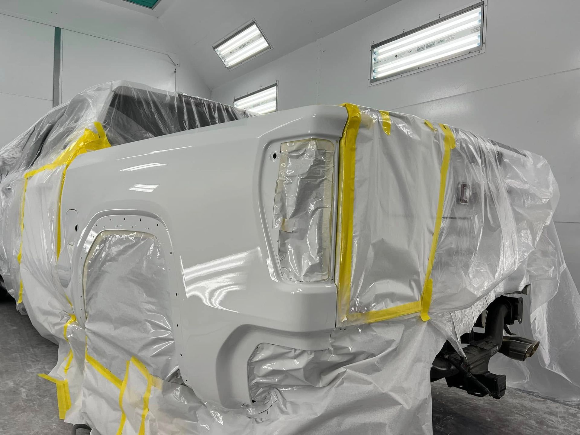 White car body wrapped in plastic and tape inside a clean auto paint booth
