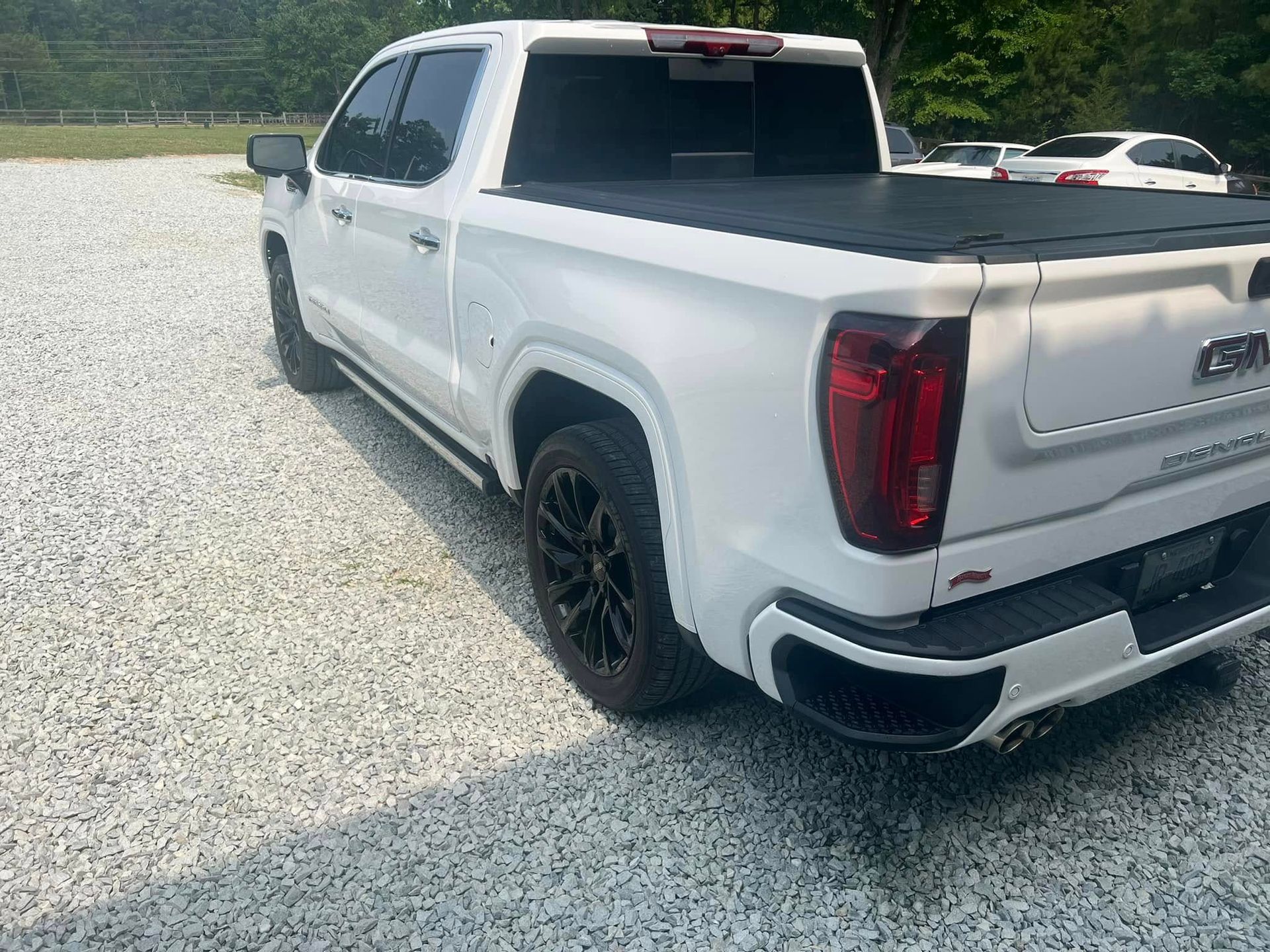White pickup truck with black rims parked on gravel in a bright outdoor lot