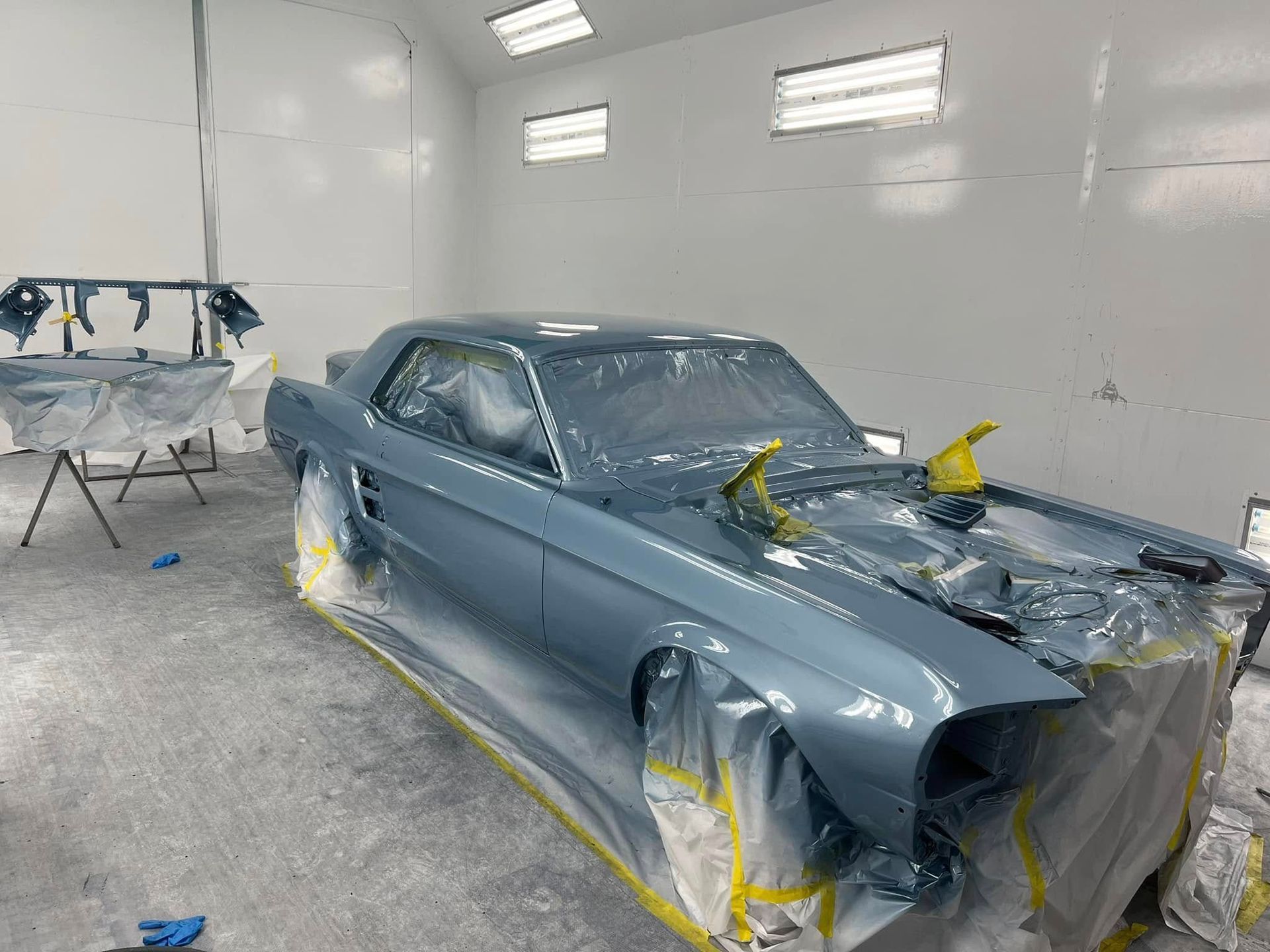 Blue classic car in a paint booth, masked with tape and plastic for restoration work
